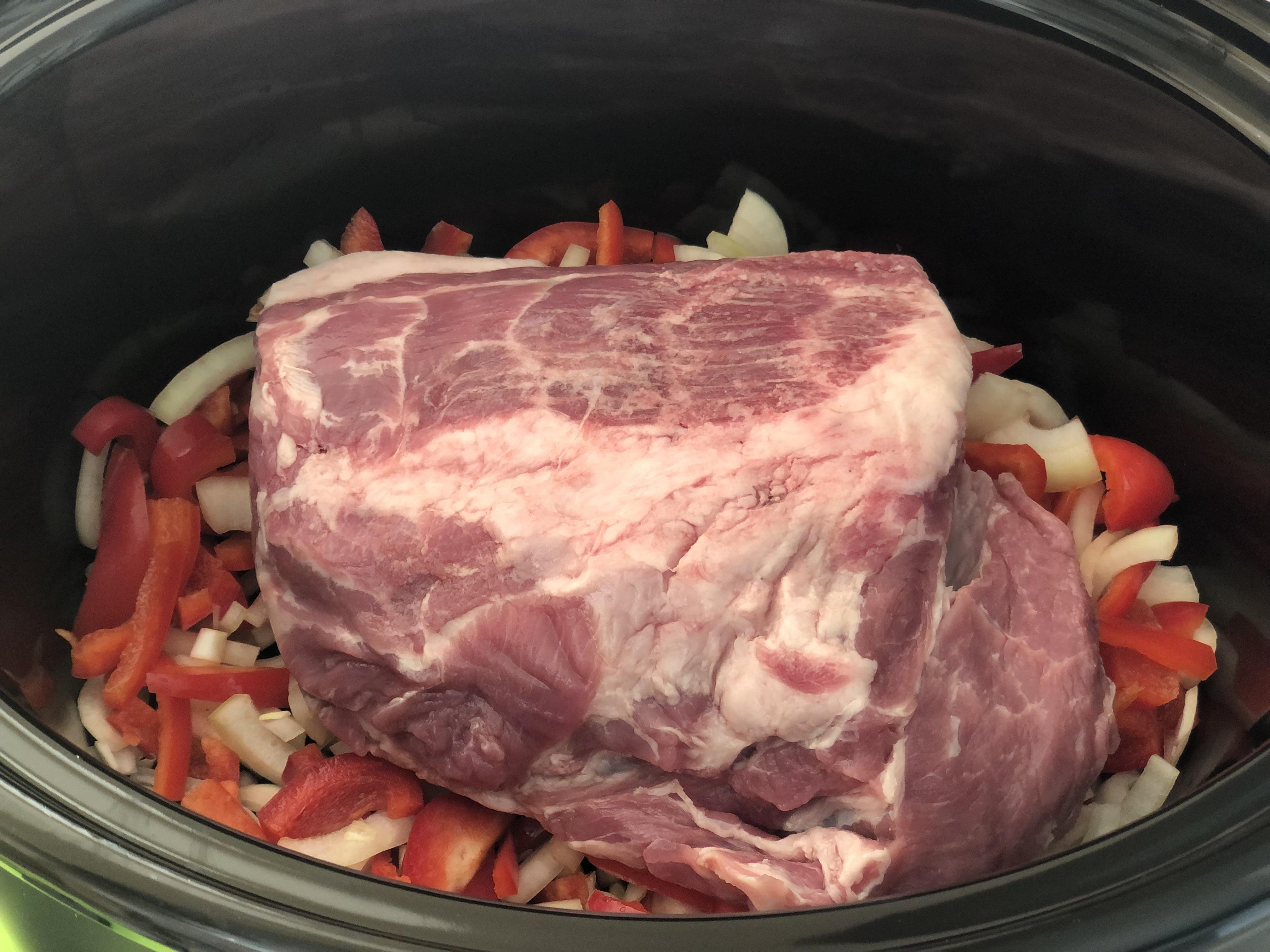 Measured ingredients for slow cooker pork shoulder including sliced onions, garlic, apple cider vinegar, ketchup, Dijon mustard, Worcestershire sauce, spices, and a pork shoulder on a kitchen counter