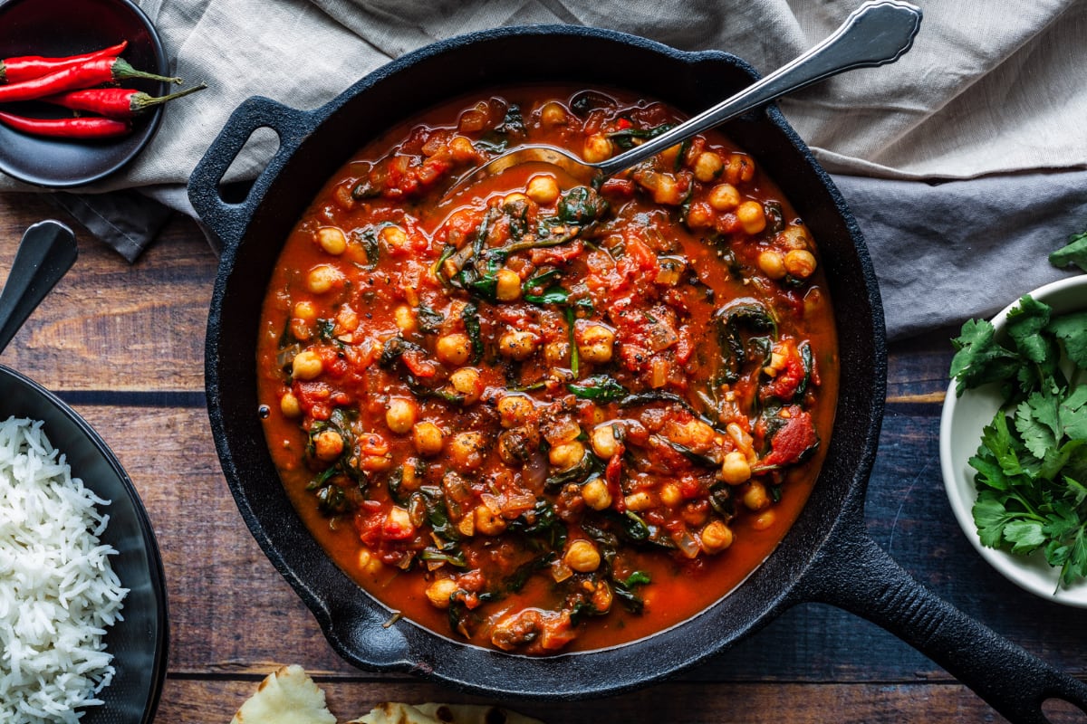 Measured ingredients on a kitchen counter including baby spinach, canned chickpeas, canned diced tomatoes, lemon, garlic, onion, olive oil, and spices in small bowls