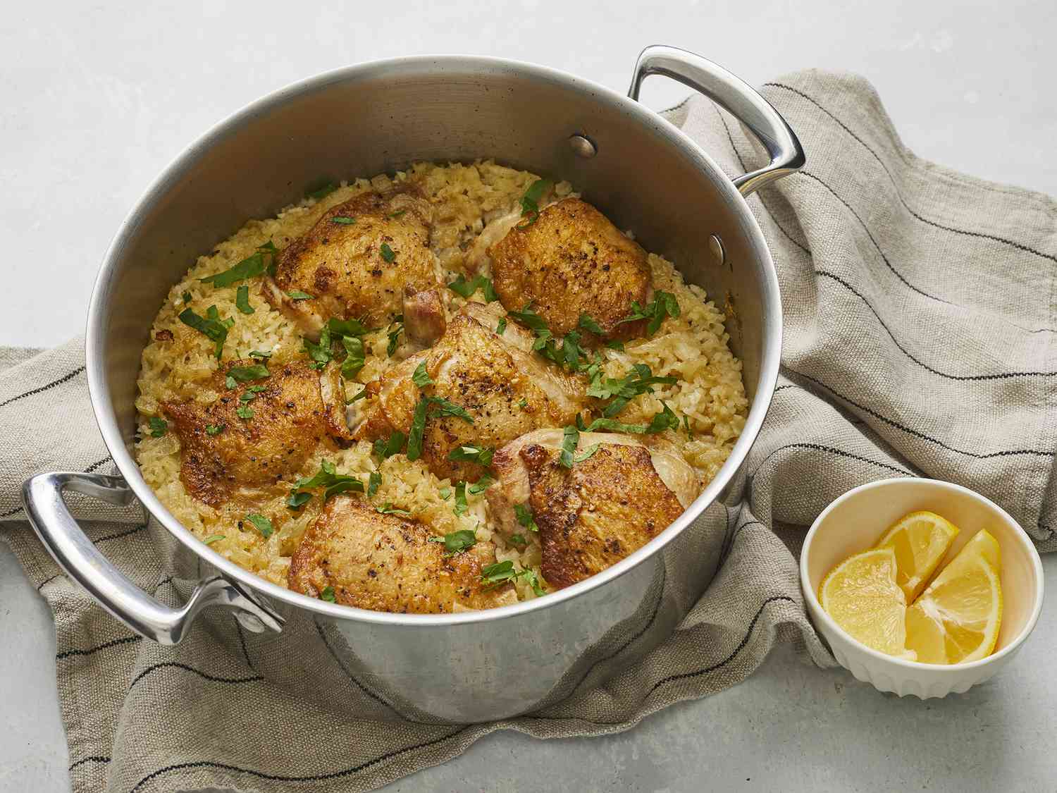 Measured ingredients on a kitchen counter including chicken thighs, rice, onion, garlic, lemon, chicken broth, parsley, yogurt, and spices arranged in small bowls