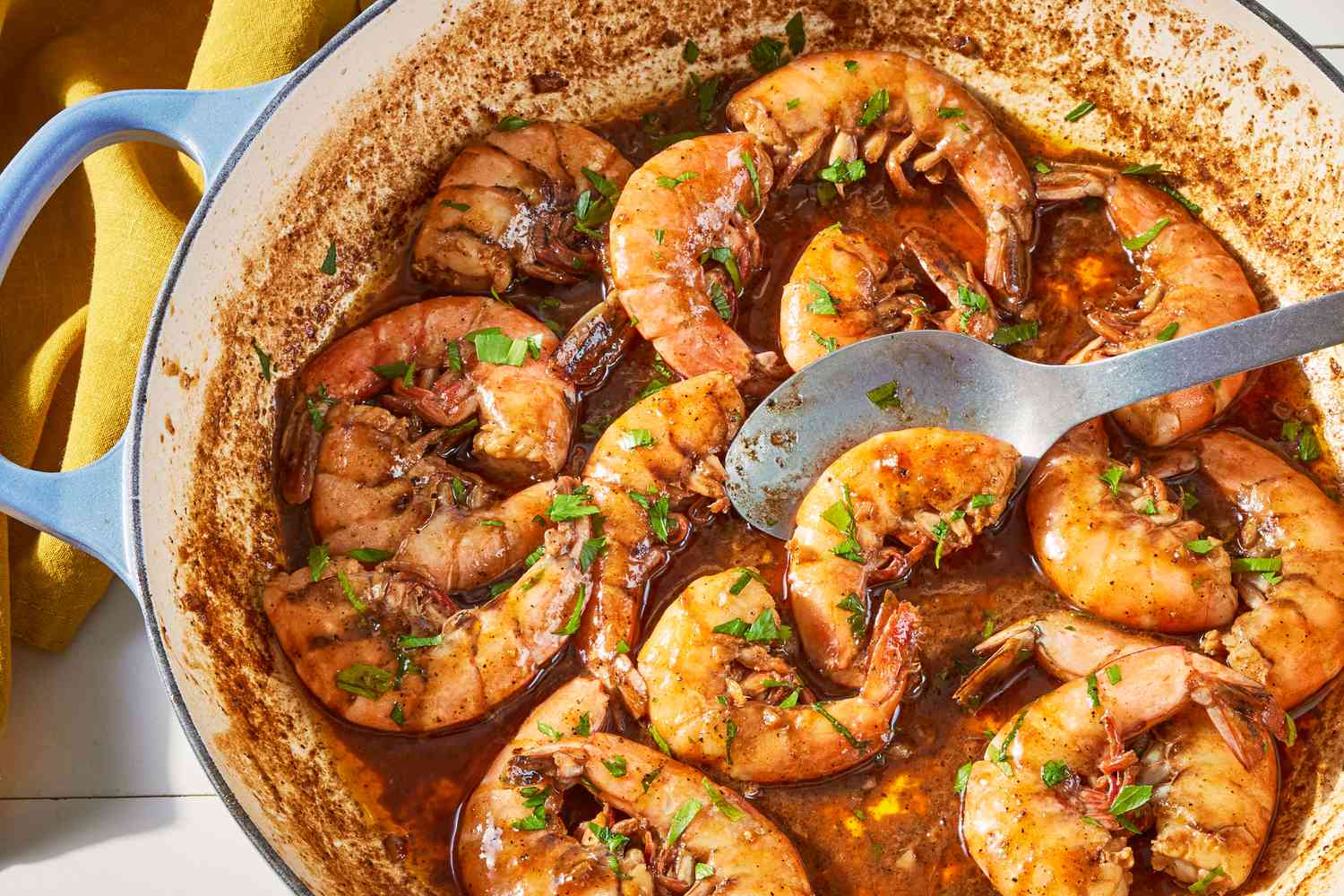 Measured spices, butter, Worcestershire sauce, BBQ sauce, and a bowl of peeled shrimp set beside a large skillet on a kitchen counter