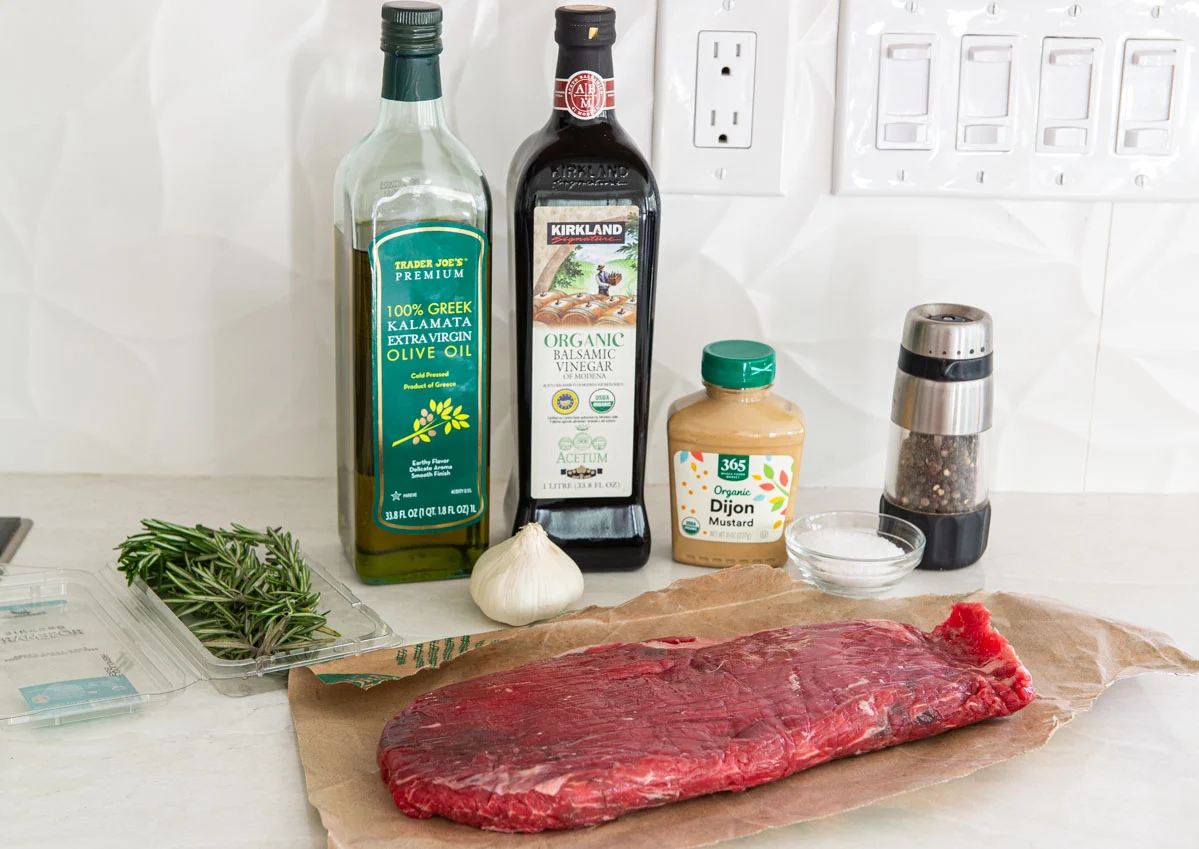 Measured steak marinade ingredients on a kitchen counter including soy sauce, Worcestershire sauce, olive oil, brown sugar, garlic, black pepper, and lemon