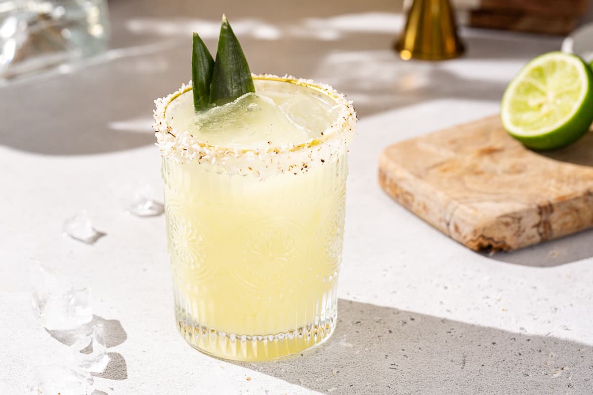 Measured tequila, pineapple juice, fresh lime juice, and orange liqueur in small glass measuring cups beside a cocktail shaker