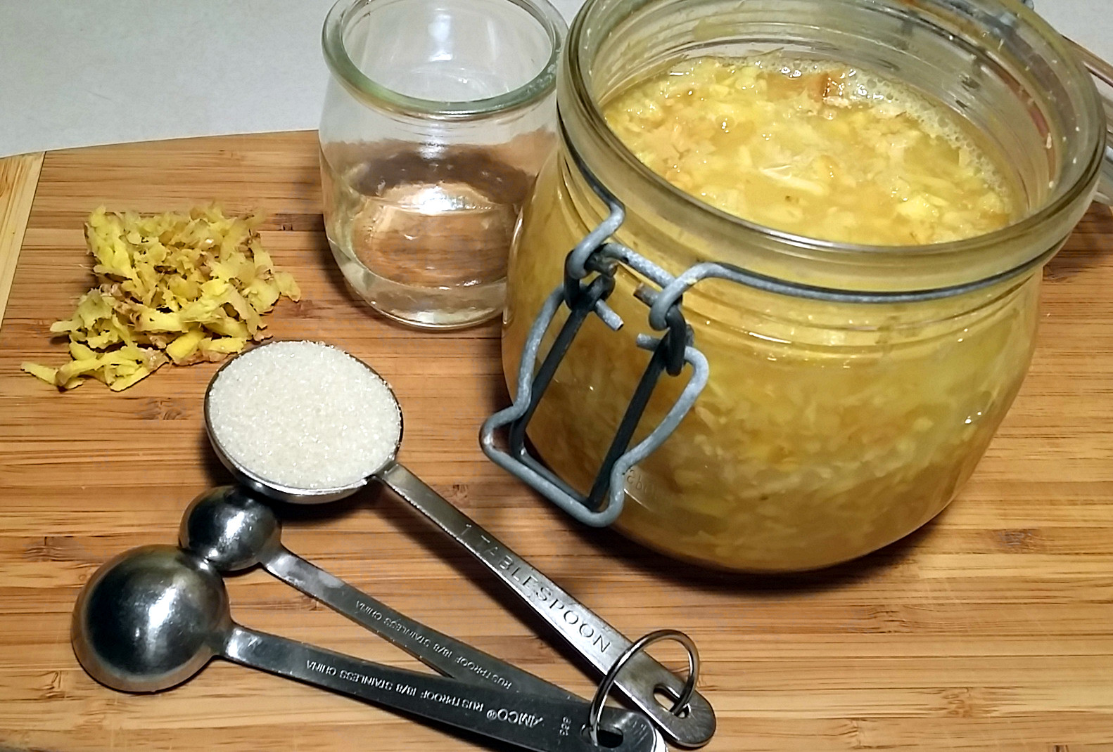 Measuring spoons holding grated ginger and sugar on a clean kitchen counter