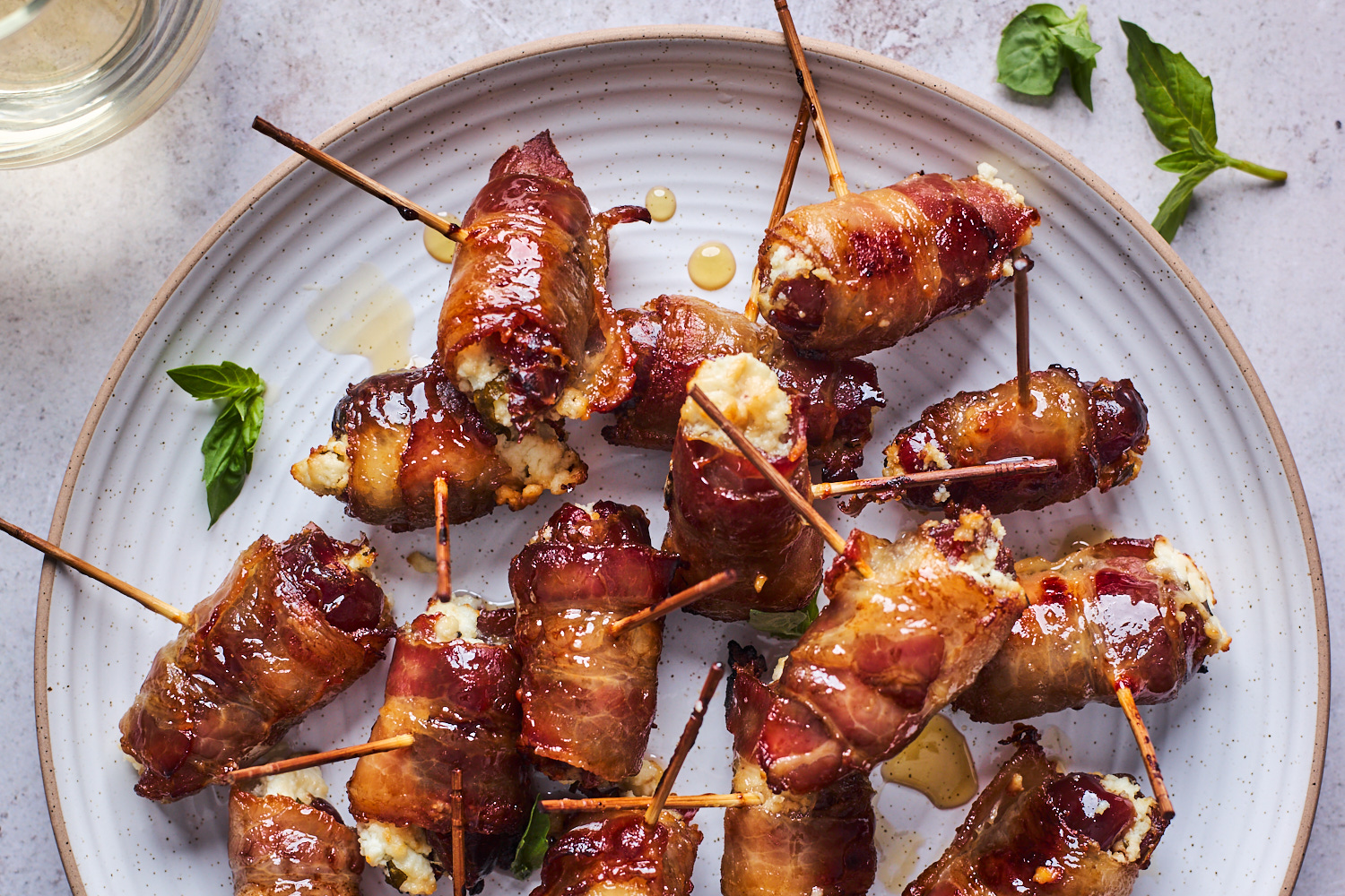 Medjool dates, bacon slices, and a bowl of goat cheese arranged on a clean kitchen counter with a cutting board and toothpicks