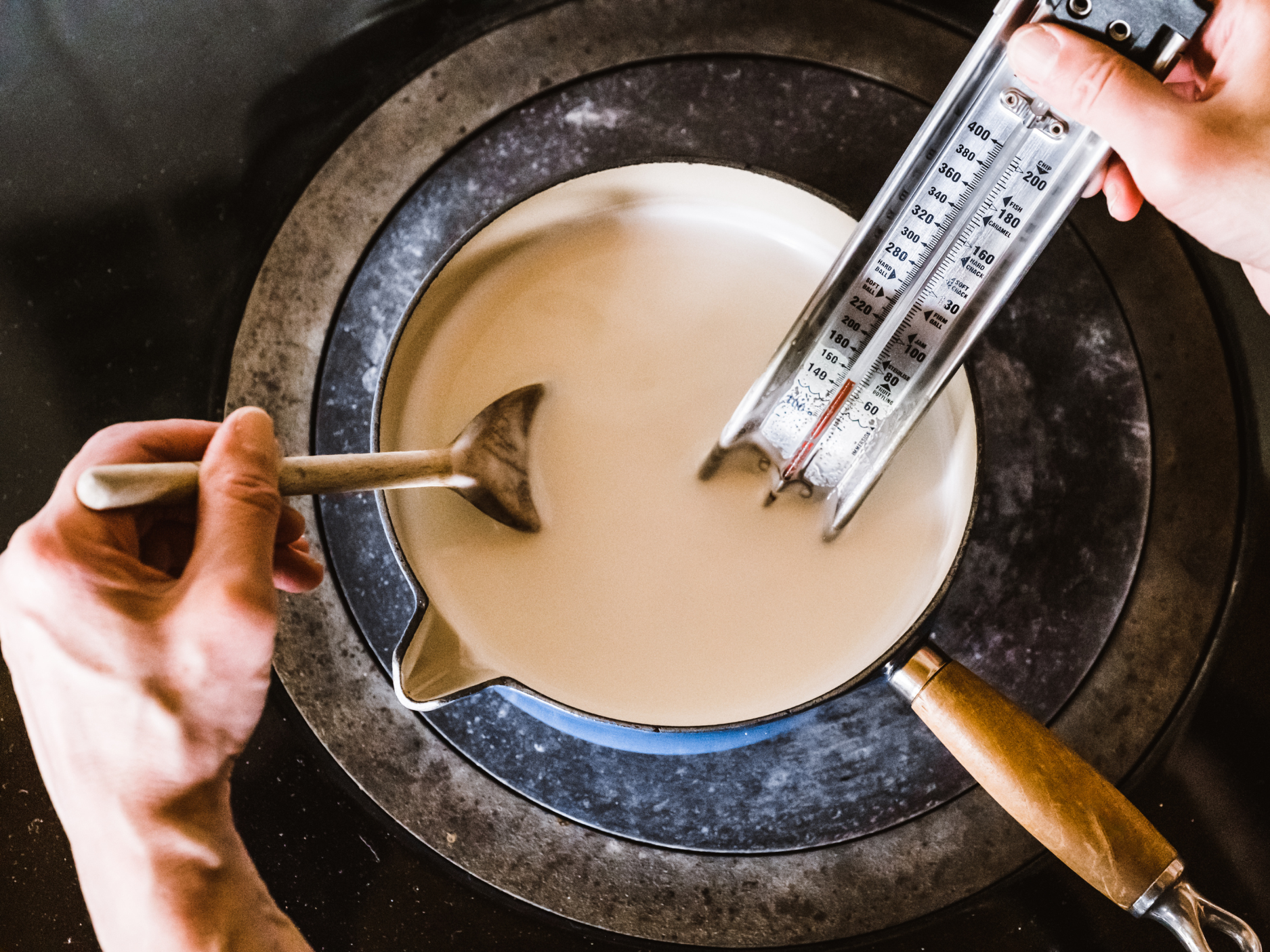 Milk, a small bowl of plain yogurt starter, a thermometer, and a whisk arranged on a clean kitchen counter
