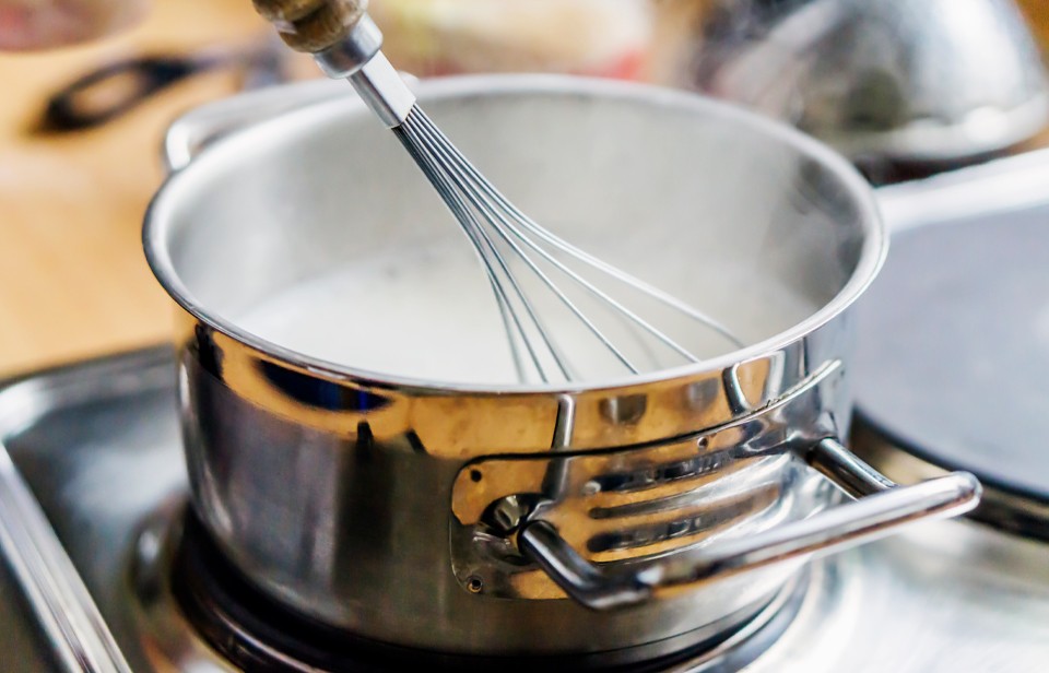 Milk and cream gently steaming in a stainless steel saucepan on a stovetop with a whisk nearby