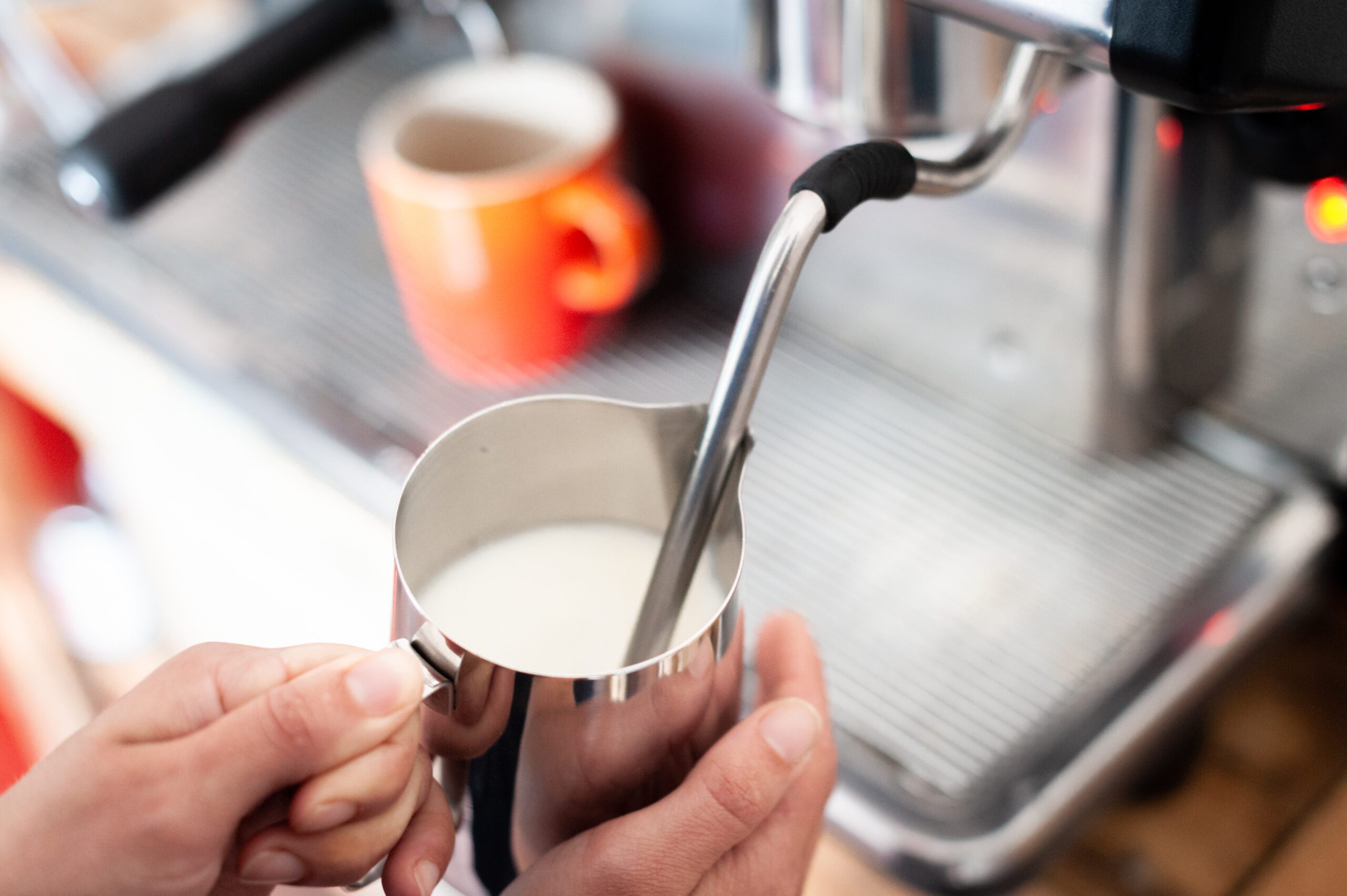 Milk being steamed in a stainless steel pitcher with a steam wand, showing a smooth whirlpool motion on a home espresso machine