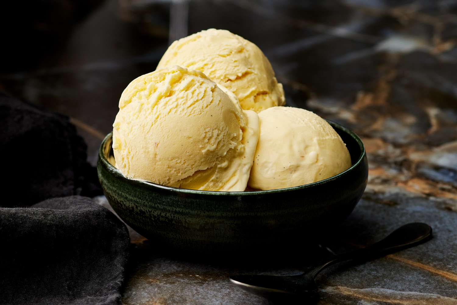 Milk, cream, sugar, egg yolks, and vanilla arranged on a clean kitchen counter with measuring cups
