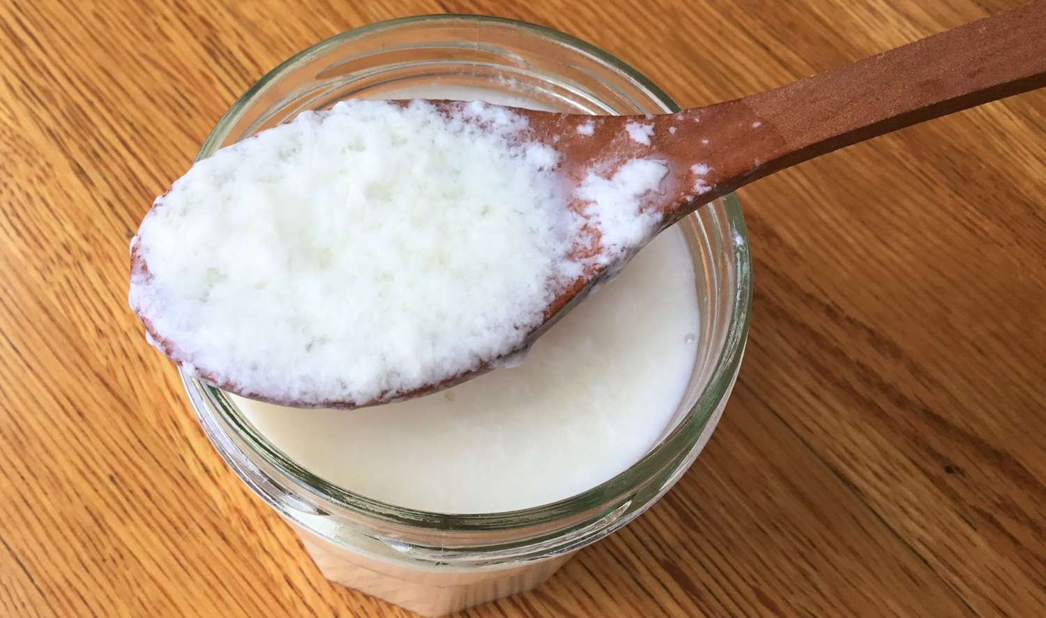 Milk with a small splash of vinegar in a glass bowl beginning to curdle slightly on a kitchen counter
