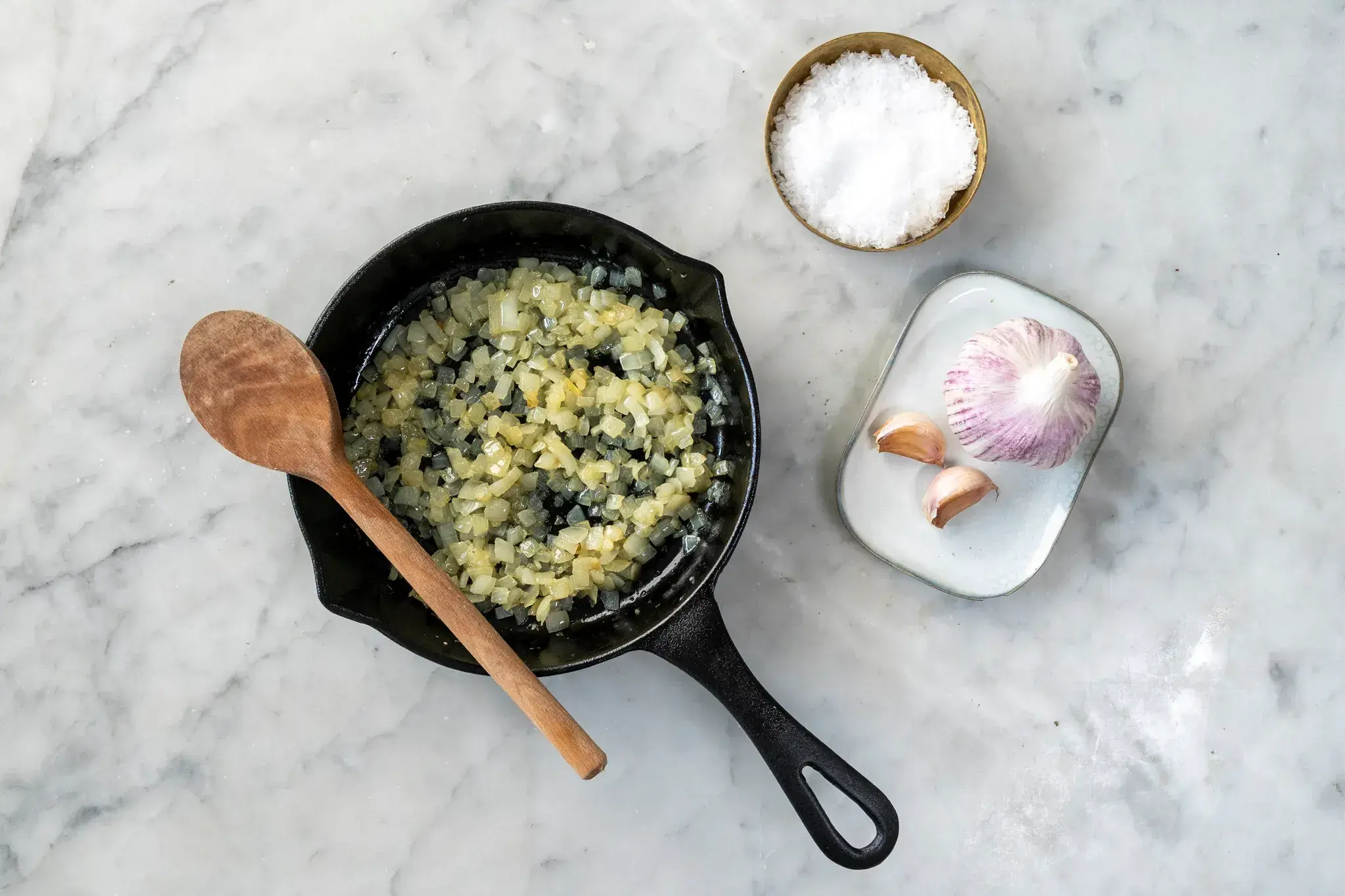 Minced garlic and diced onion sautéing in olive oil in a skillet on a stovetop