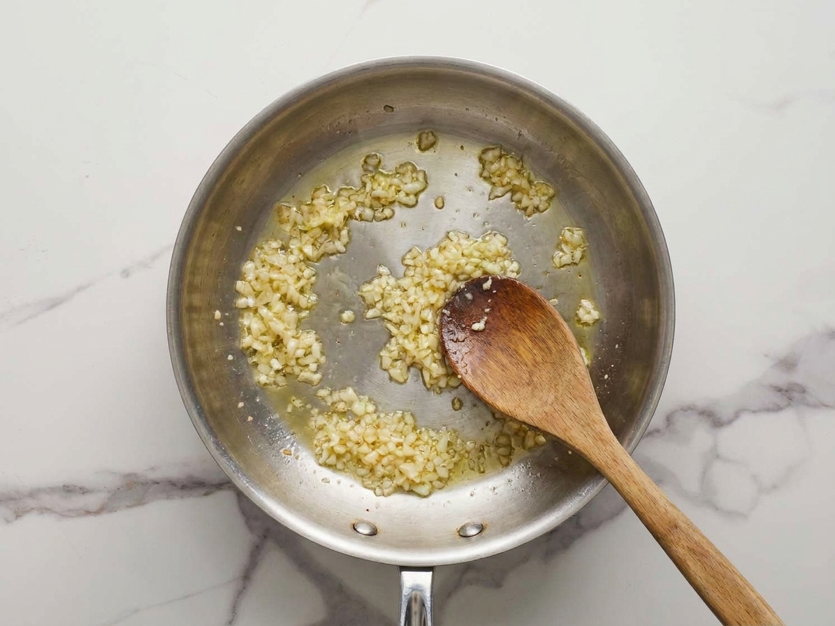 Minced garlic gently frying in a small skillet until pale golden, with a spoon stirring to prevent burning