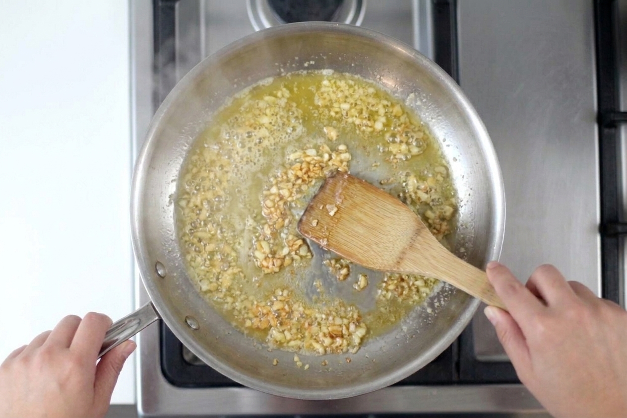 Minced garlic sizzling in melted butter in a skillet on a stovetop, being stirred until fragrant