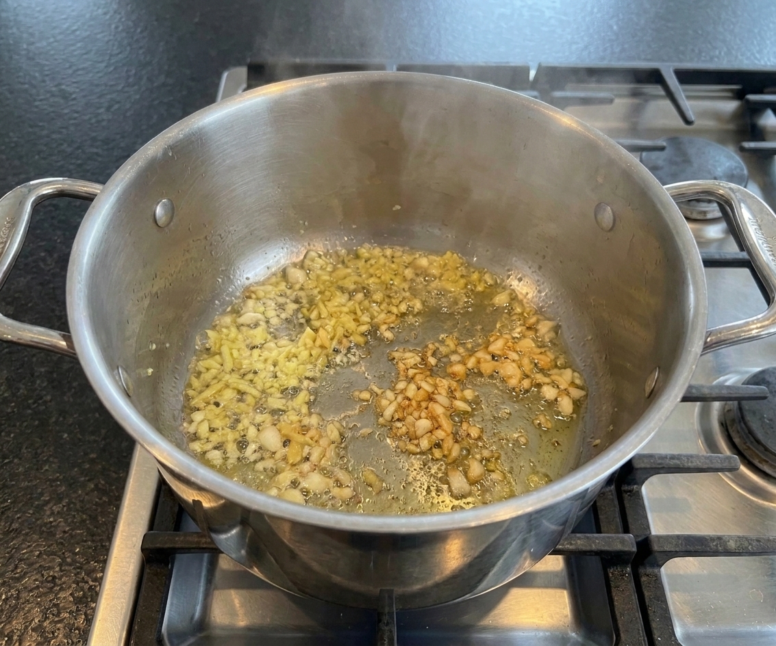 Minced ginger and garlic sizzling in oil in a saucepan before rice is added, photographed on a stovetop