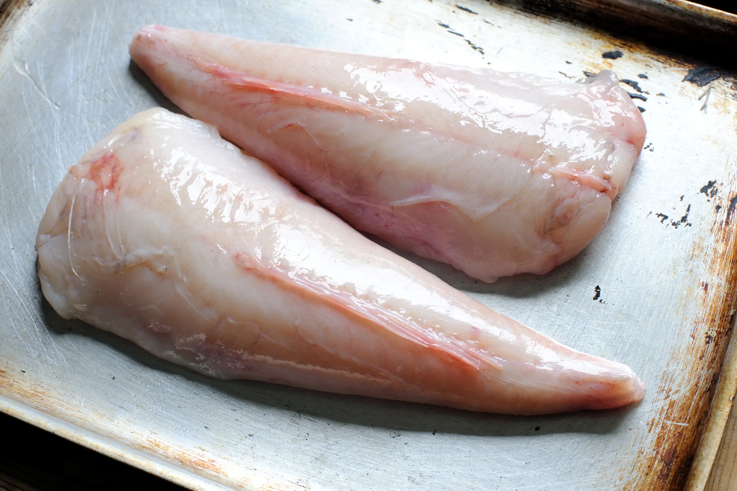 Monkfish tail meat portioned into thick pieces on a cutting board with a knife and paper towels nearby on a home kitchen counter