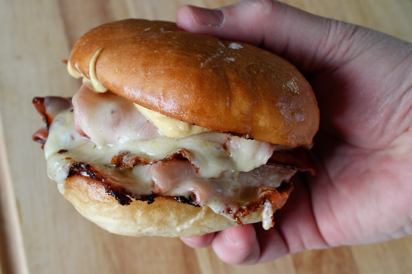 Mortadella slices, provolone, a kaiser roll, mayonnaise, and mustard arranged on a wooden cutting board on a bright kitchen counter