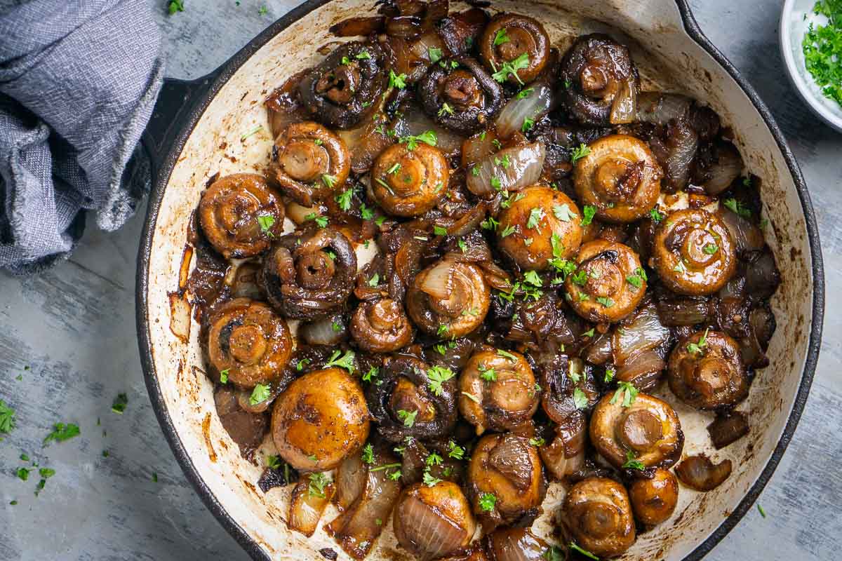 Mushrooms and sliced onions sautéing in a wide skillet on a stovetop, turning golden at the edges
