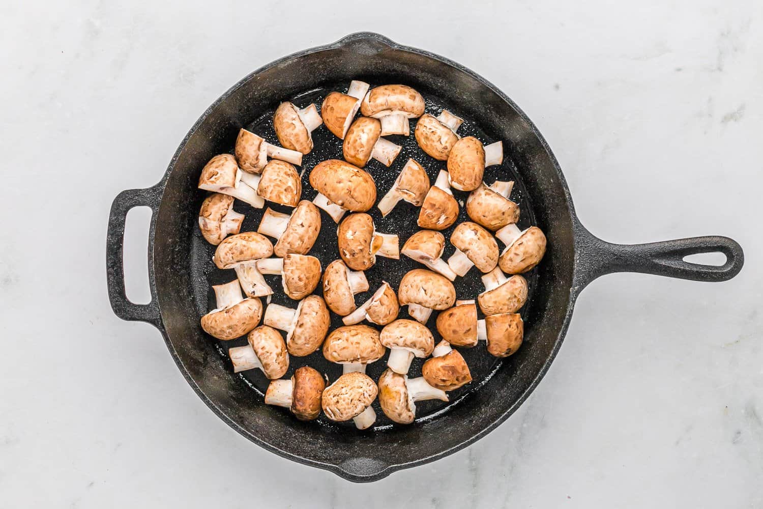 Mushrooms spread in a single layer in a hot skillet with space between pieces, beginning to cook as moisture starts to appear