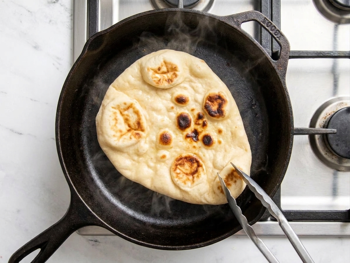 Naan being reheated in a cast iron skillet until warm and pliable, with browned bubbles visible
