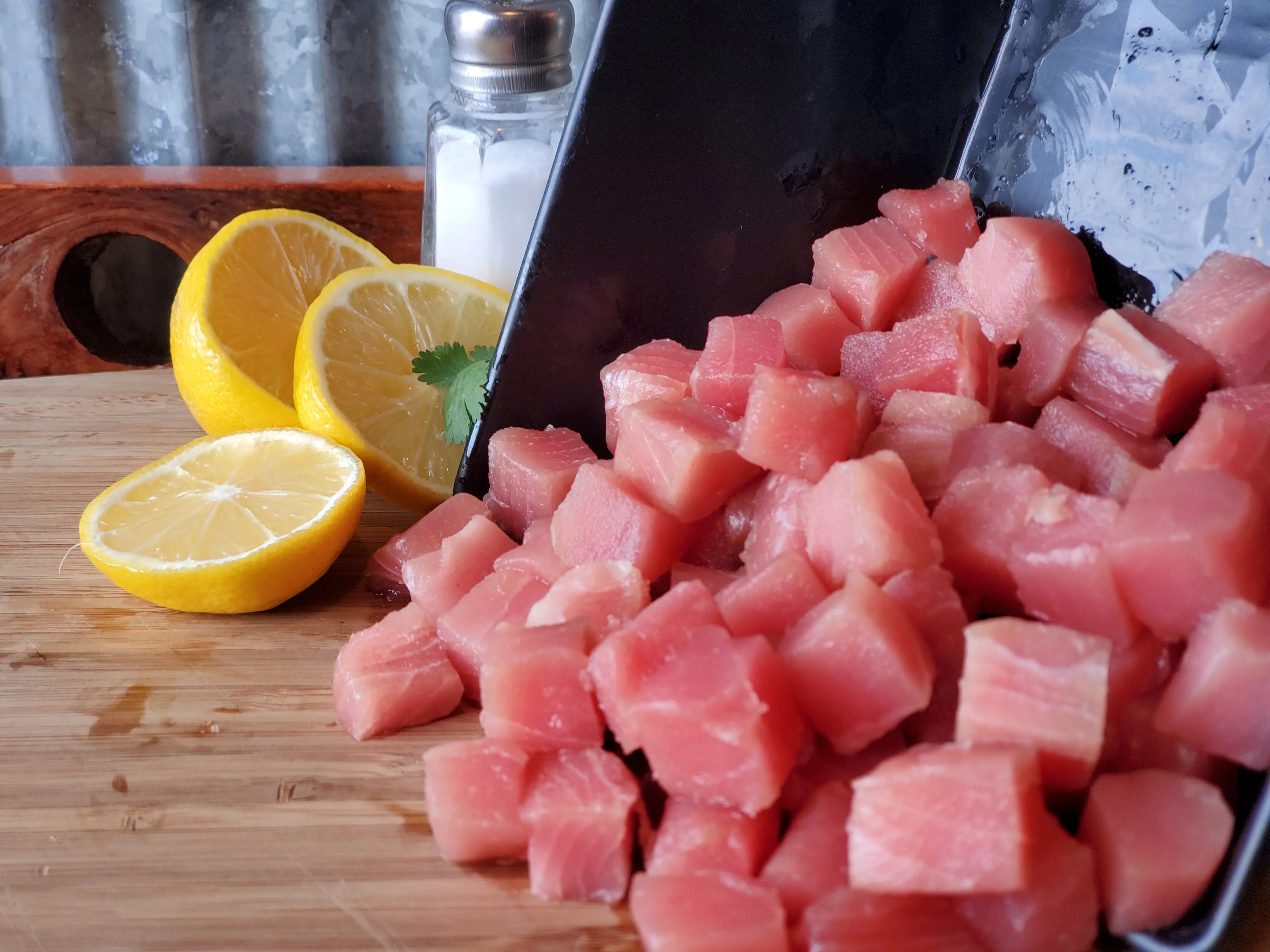 Neatly cubed raw tuna on a wooden cutting board with a chef's knife on a bright kitchen counter