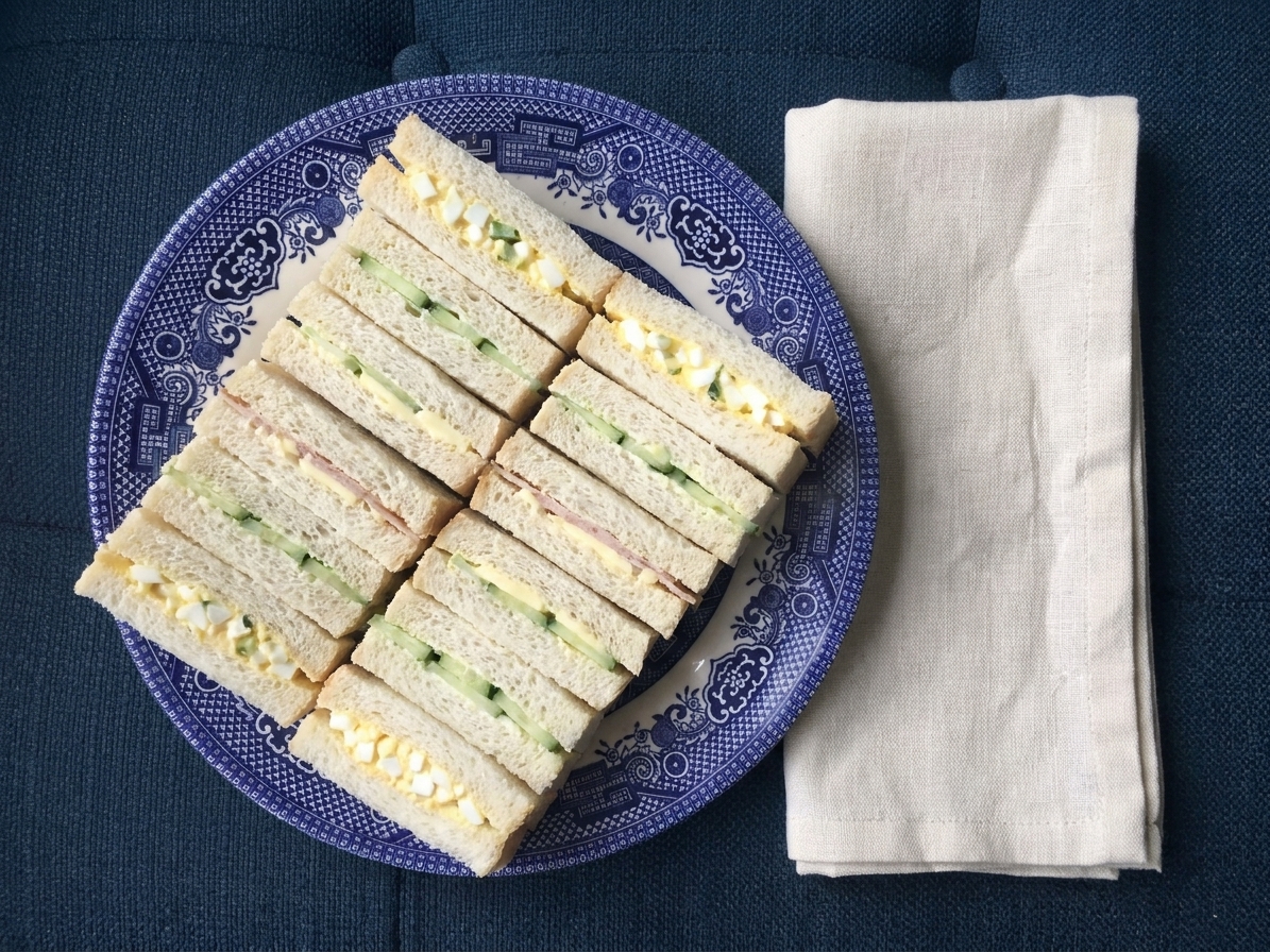 Neatly sliced finger sandwiches arranged in rows on a serving platter with a simple linen napkin on the table