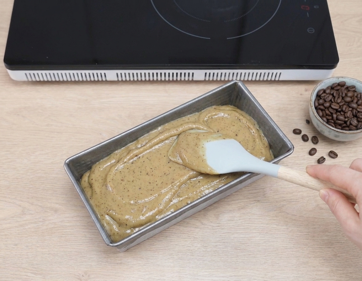No-churn coffee ice cream mixture smoothed into a loaf pan with a spatula on a kitchen counter