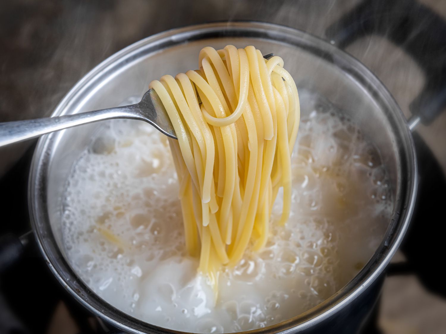 Noodles boiling in a stainless steel saucepan on a home stove, with steam rising under warm kitchen lighting