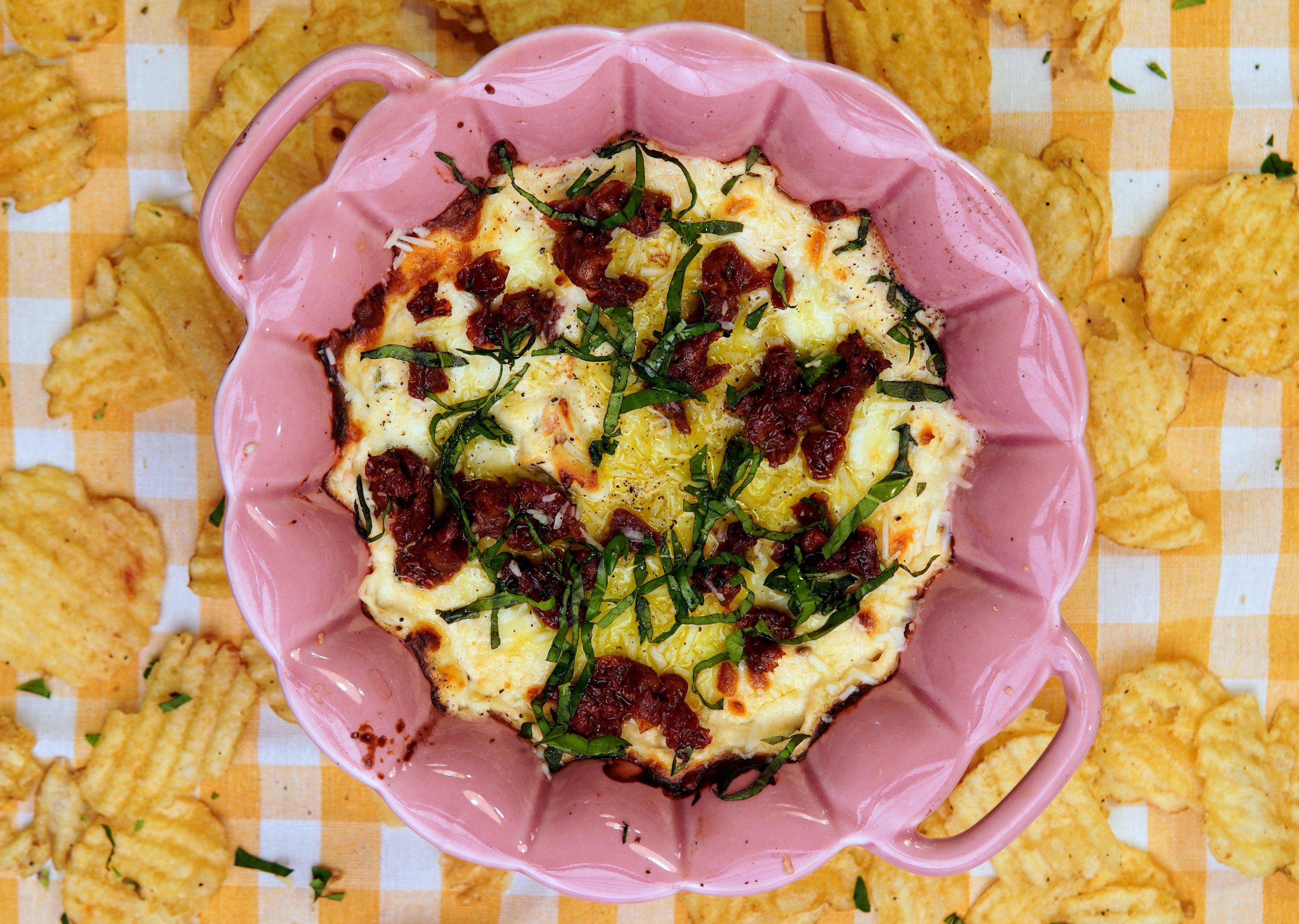 Oil-packed sun-dried tomatoes, garlic cloves, Parmesan cheese, nuts, lemon, and olive oil arranged on a clean kitchen counter