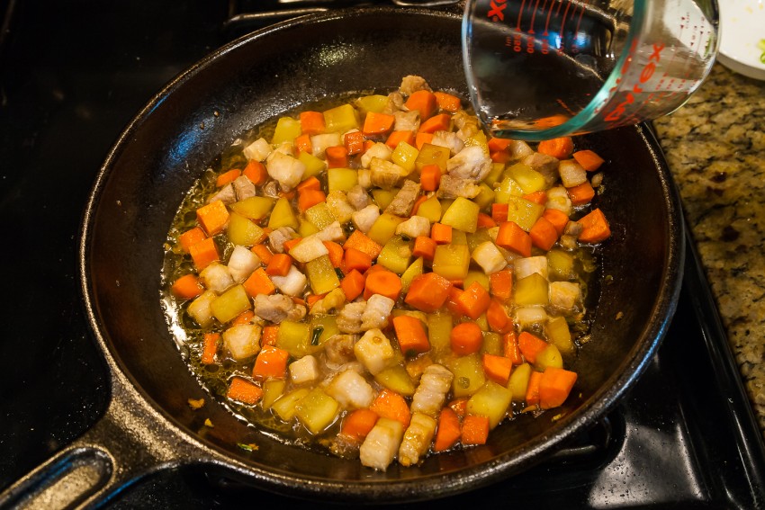 Onion and carrot slices cooking in a saucepan on a stovetop, lightly glossy with oil and beginning to soften