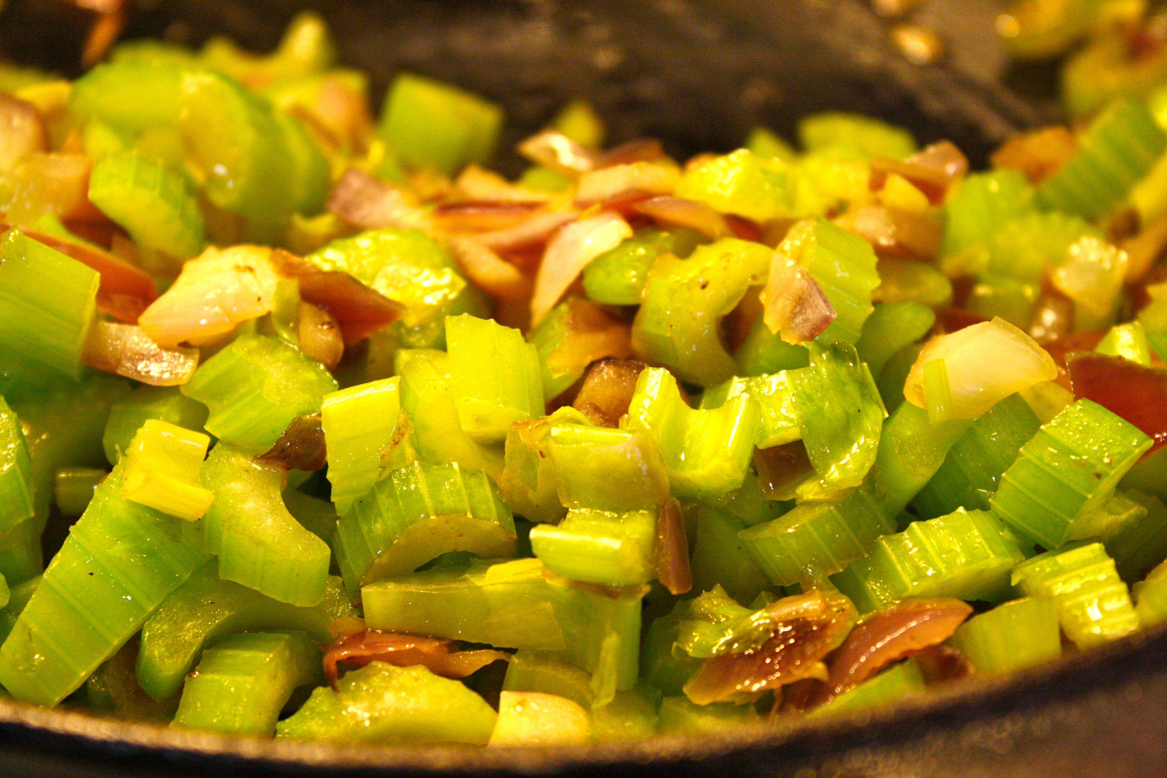 Onion and celery sautéing in melted butter in a skillet on a stovetop, turning soft and translucent