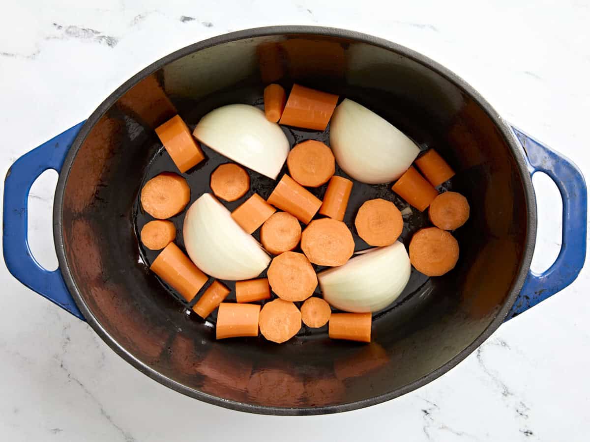 Onion and diced carrots sautéing in a Dutch oven on a stovetop with a wooden spoon