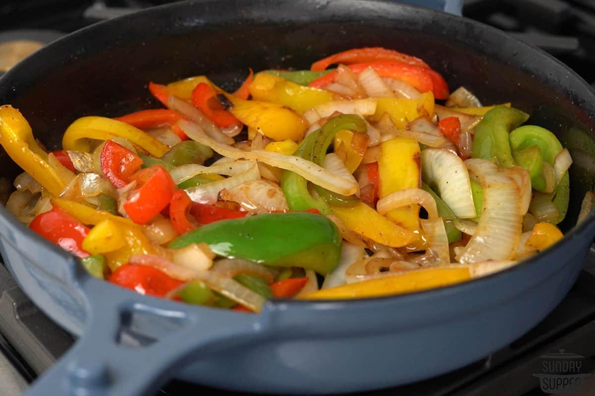 Onion and diced green bell pepper sautéing in a Dutch oven on a stovetop with a wooden spoon stirring