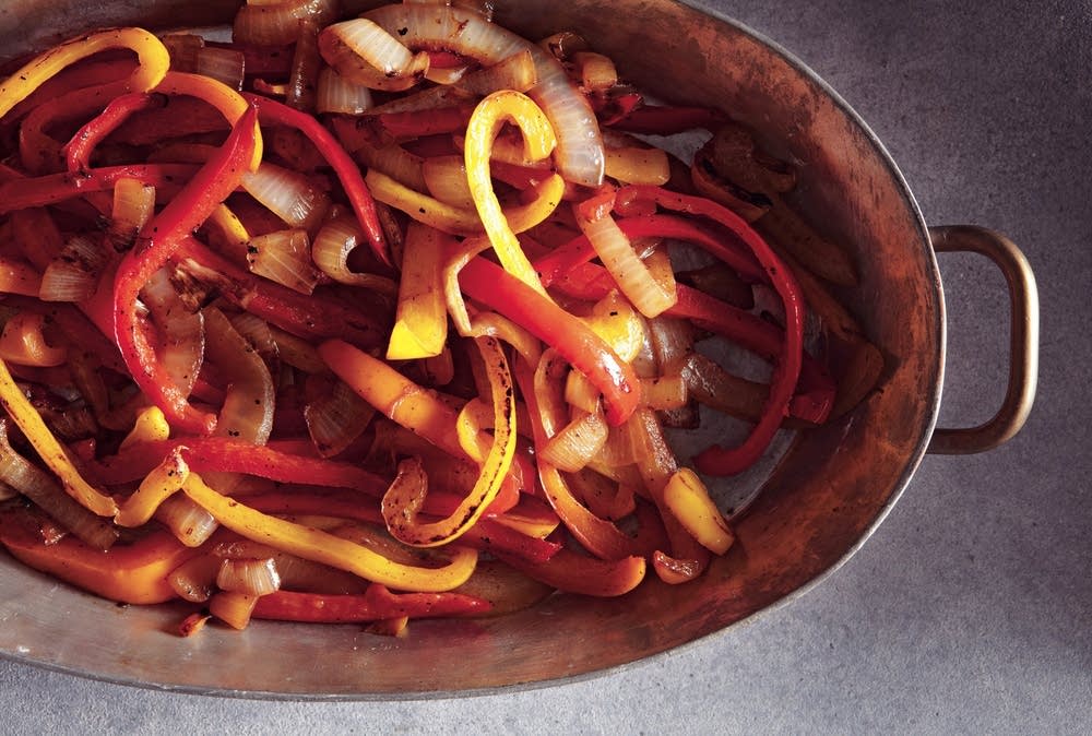 Onion and red bell pepper being sautéed in a skillet with olive oil on a stovetop, wooden spoon stirring