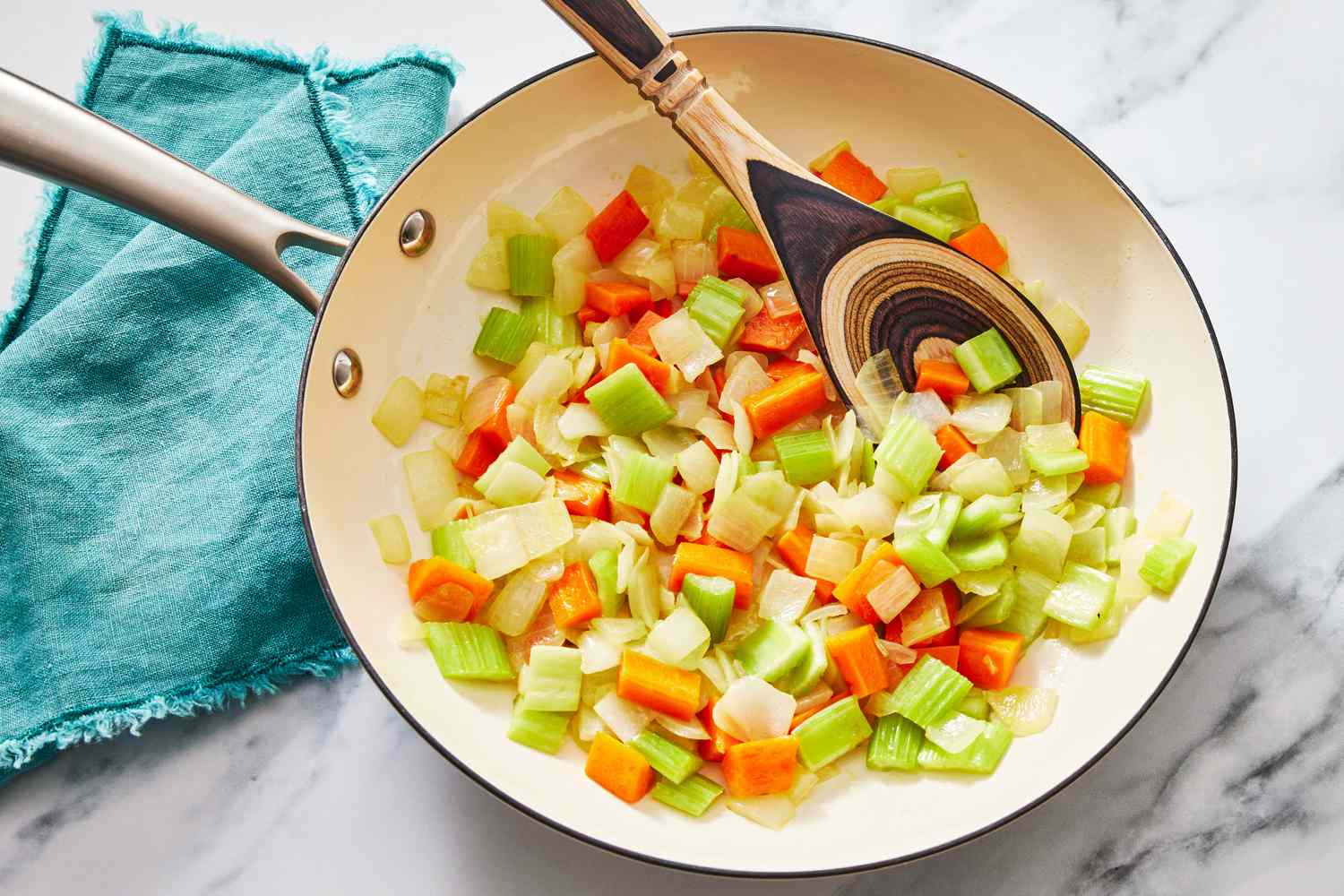Onion, carrots, and celery sautéing in a Dutch oven on a stovetop, vegetables turning glossy and tender