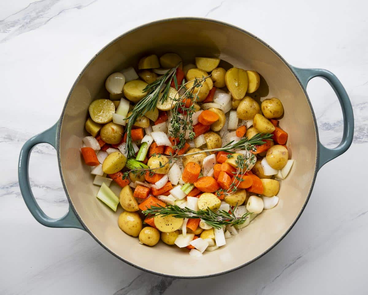Onion, carrots, and celery sautéing in a Dutch oven on a stovetop with a wooden spoon