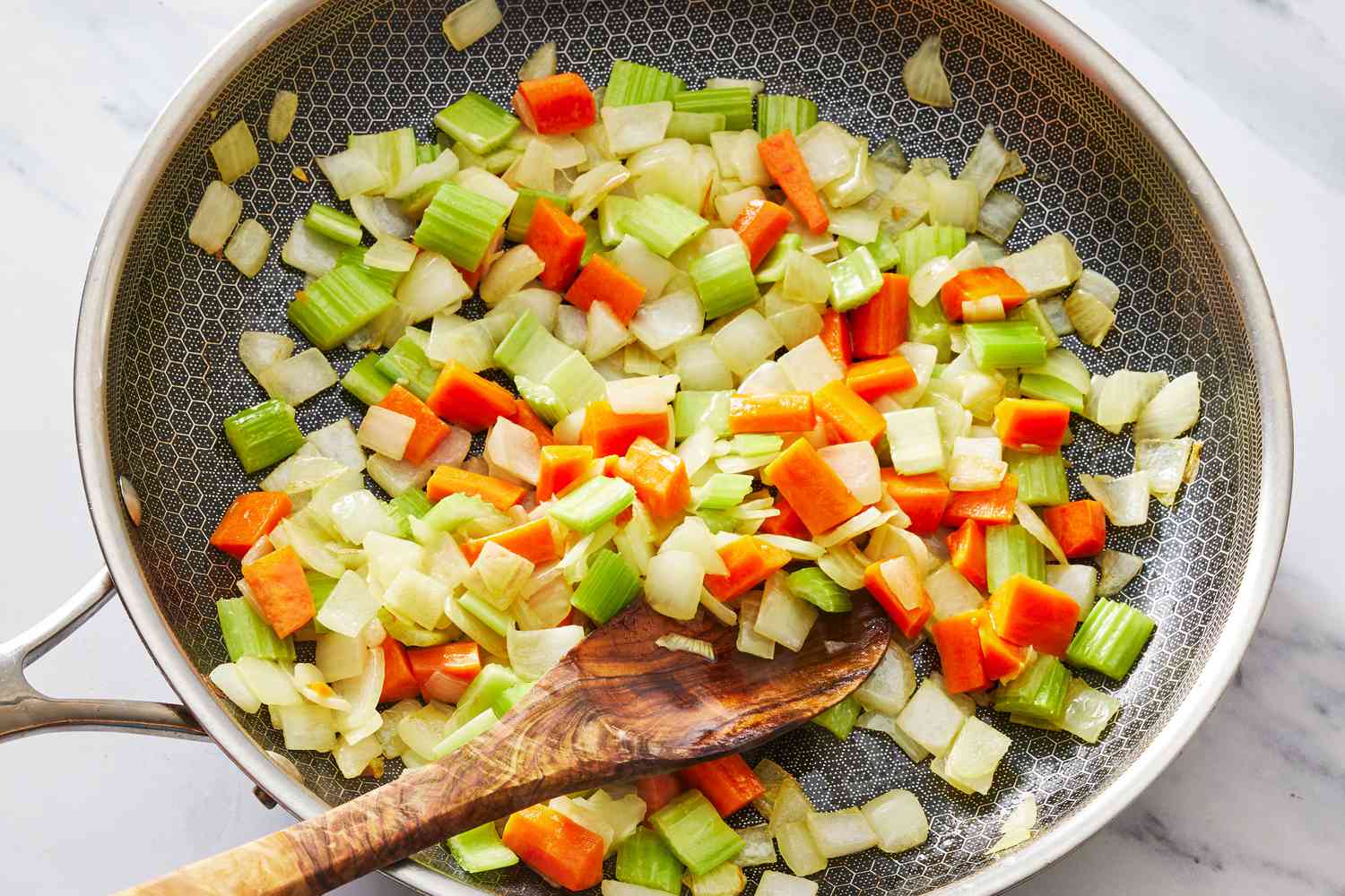 Onion, diced carrot, and celery sautéing in a Dutch oven on a stovetop with a wooden spoon stirring