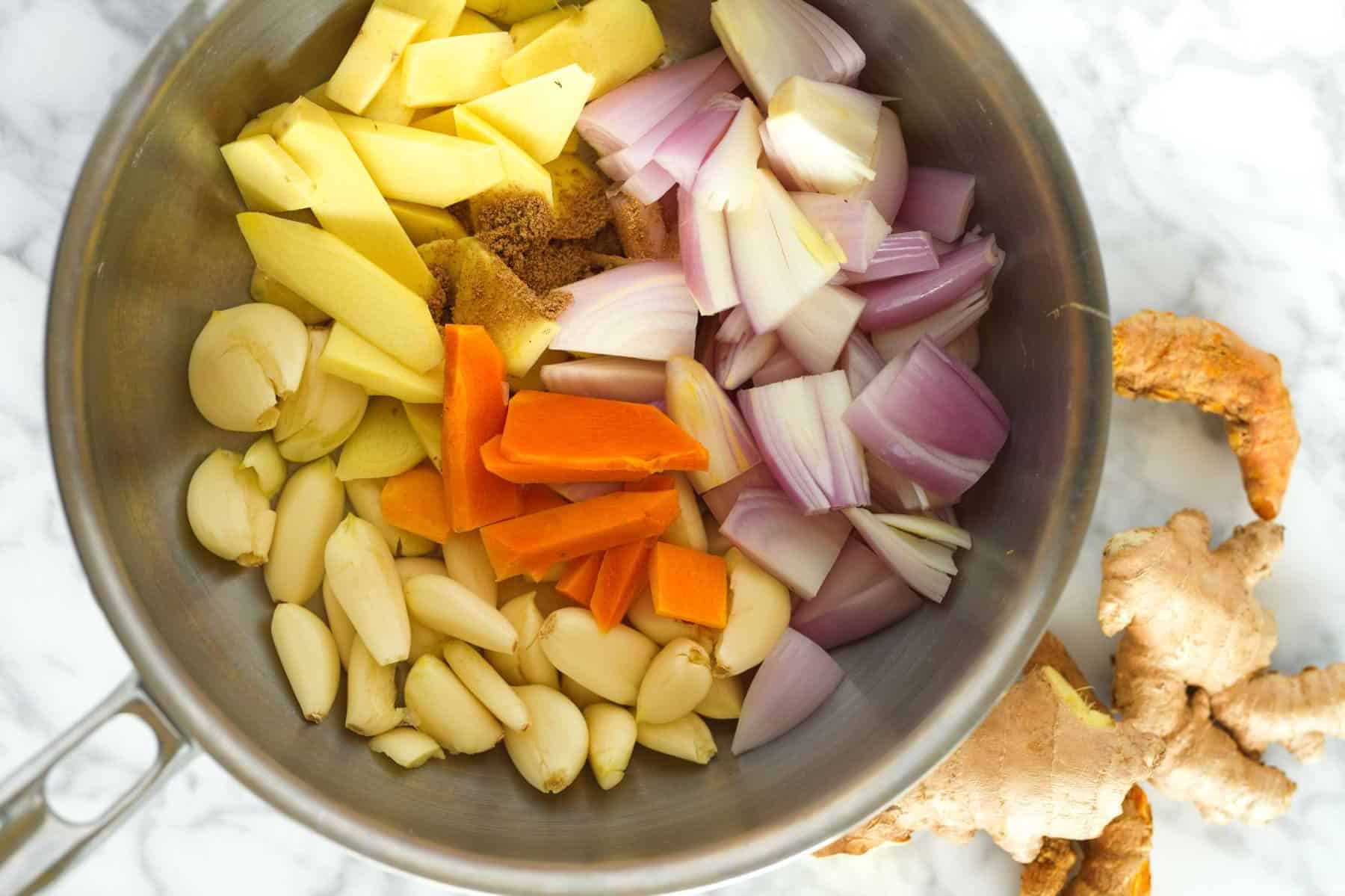 Onion, garlic, ginger, yellow curry paste, coconut milk, potatoes, carrots, chicken, and cilantro laid out on a clean kitchen counter
