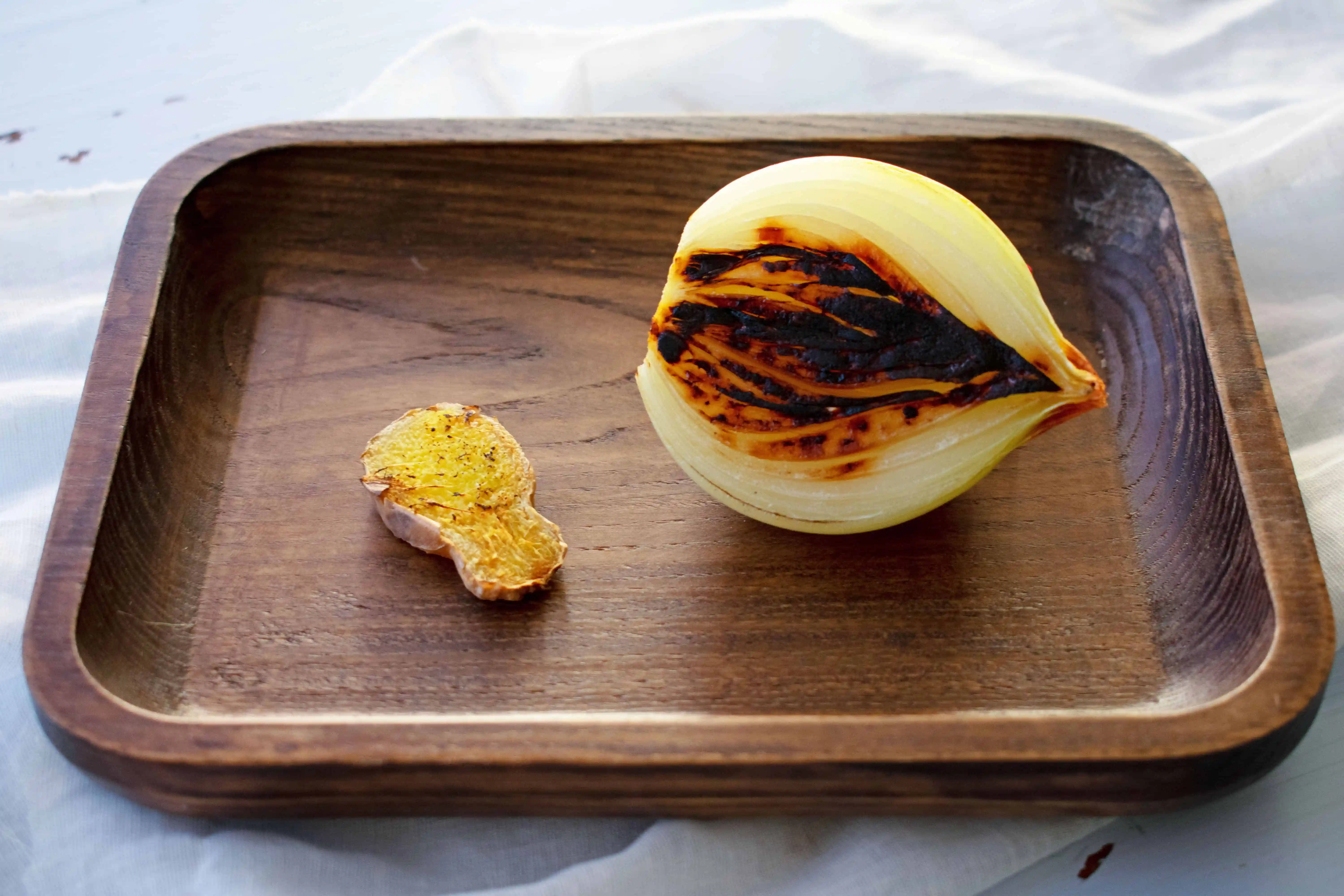 Onion halves and split ginger charring directly over a gas burner flame on a home stovetop