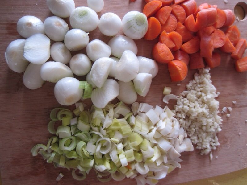 Onion quarters, carrot chunks, and celery pieces prepped on a wooden cutting board beside a halved head of garlic