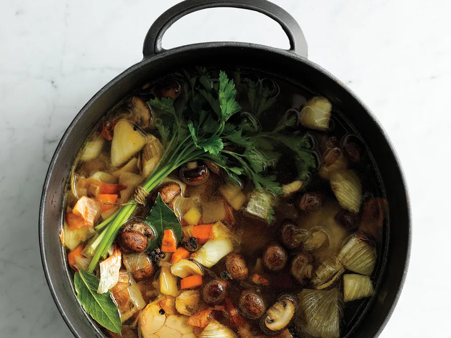 Onion quarters, carrot chunks, and celery pieces sautéing in a large stainless steel stockpot on a stovetop