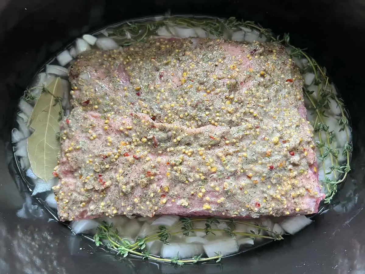 Onion quarters, smashed garlic cloves, bay leaves, and pickling spice arranged next to a corned beef brisket on a cutting board