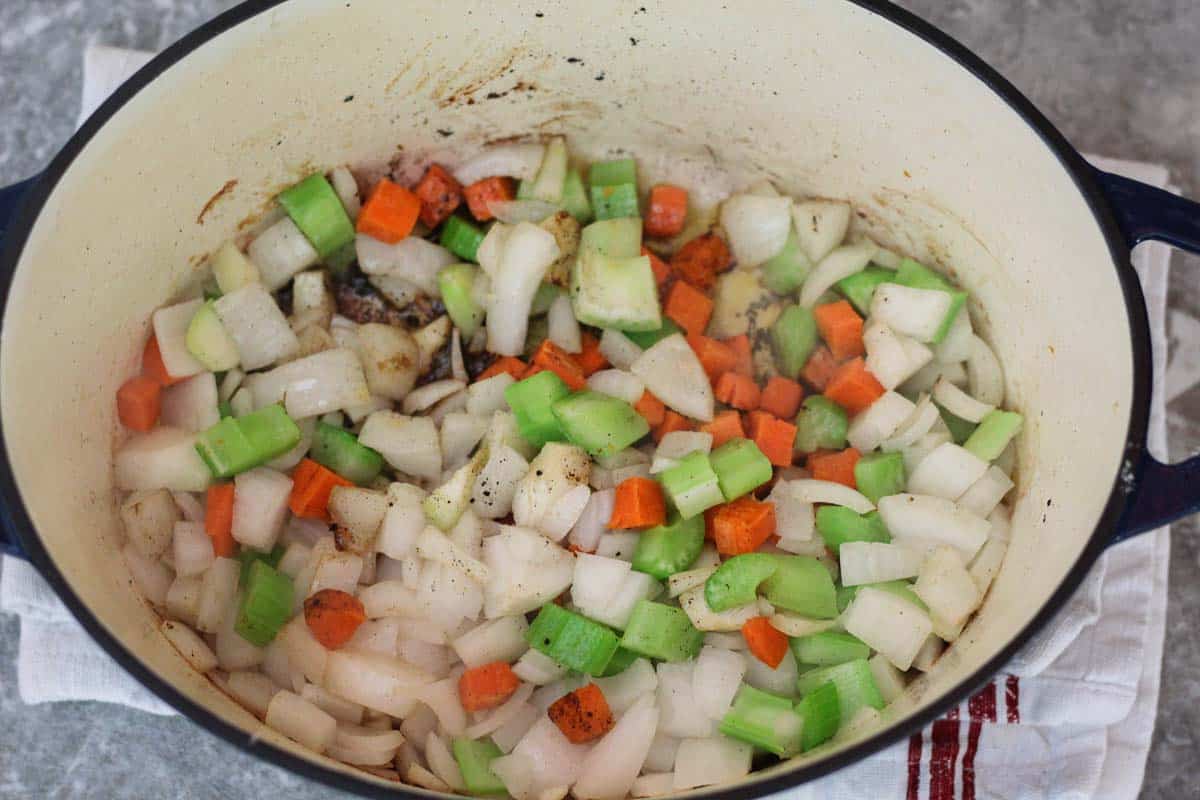 Onions, carrots, and celery sautéing in a Dutch oven on the stovetop while being stirred with a wooden spoon