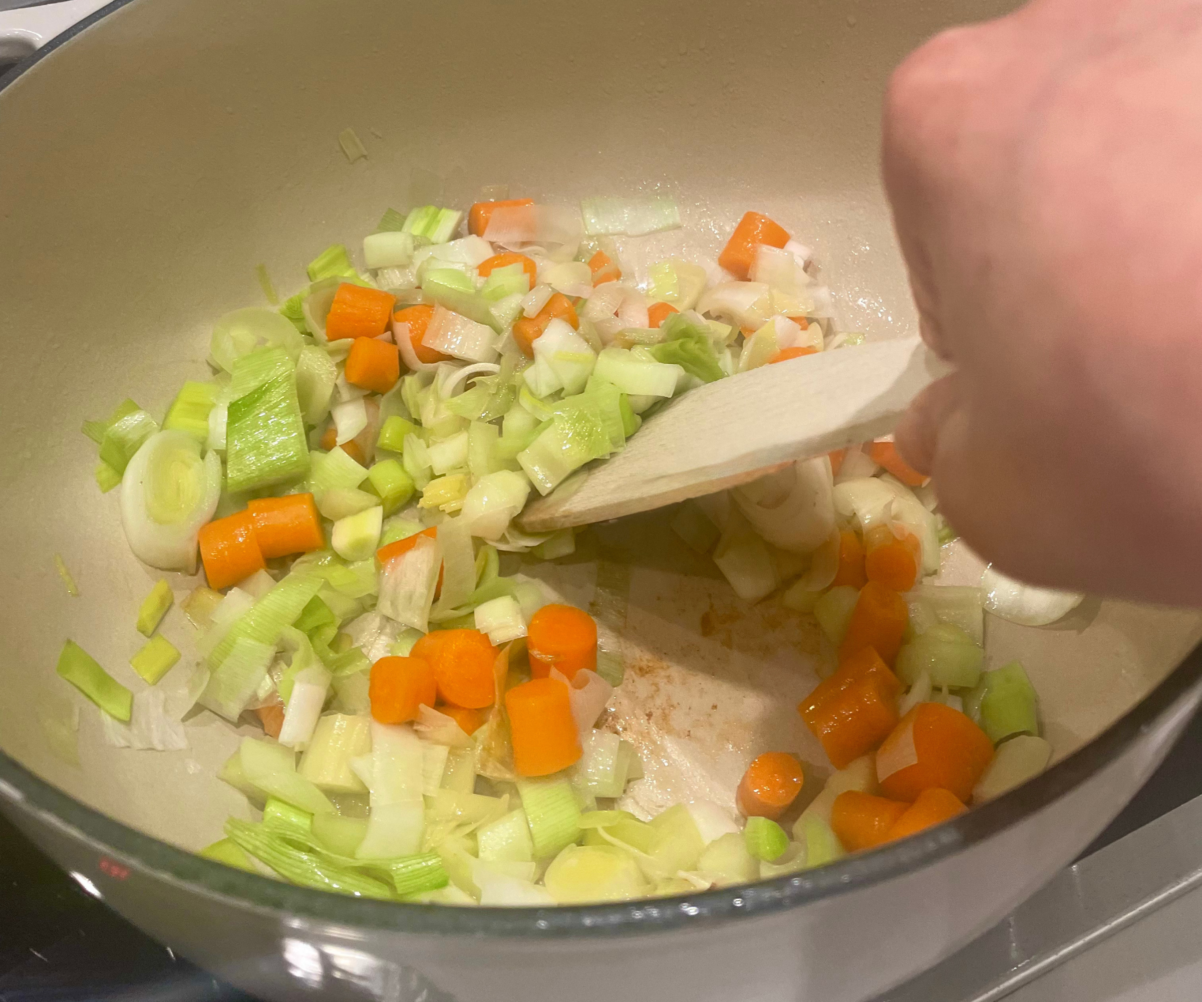 Onions, carrots, and celery sautéing in a large Dutch oven on a stovetop with a wooden spoon stirring