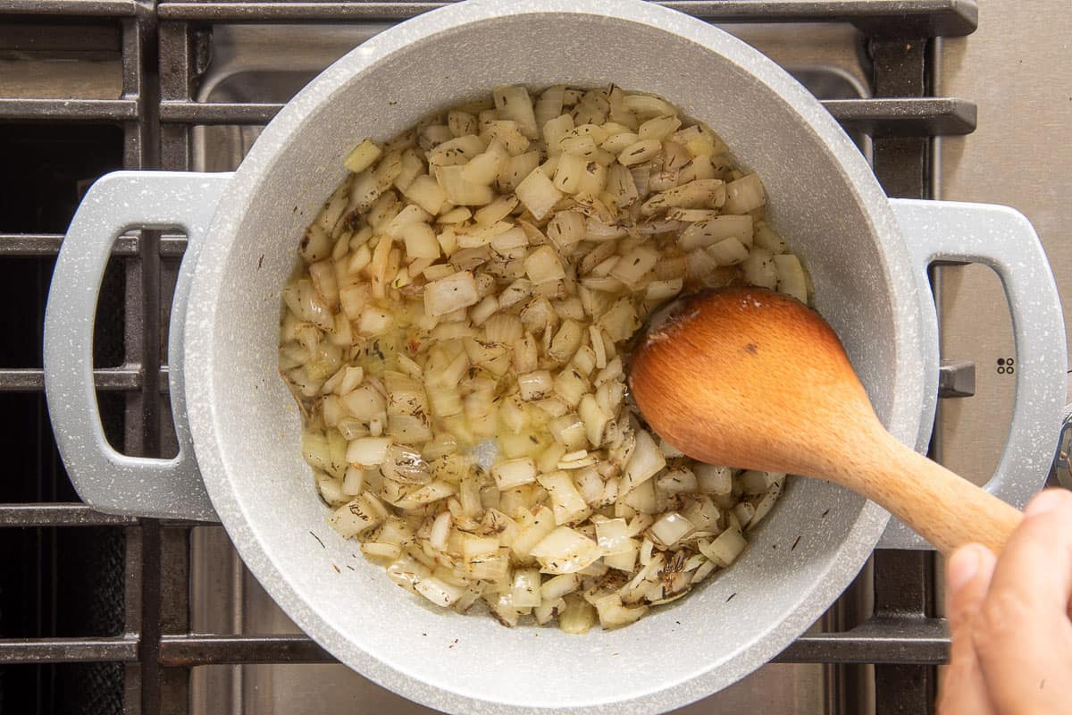 Onions sautéing in a Dutch oven on a stovetop with a wooden spoon stirring