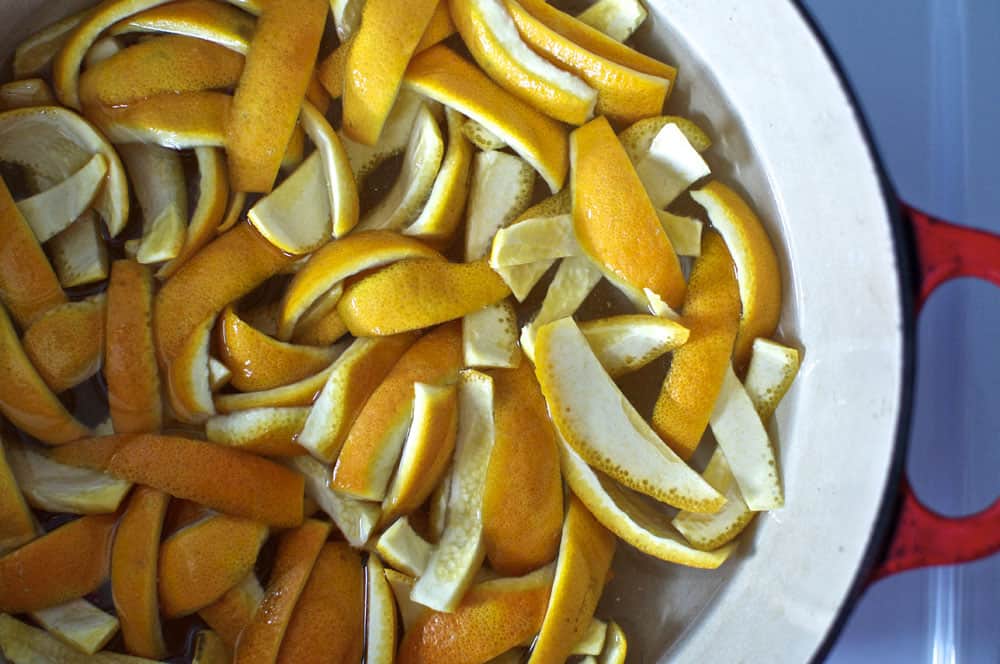 Orange peel strips simmering in a small pot of water on a stovetop during the blanching step