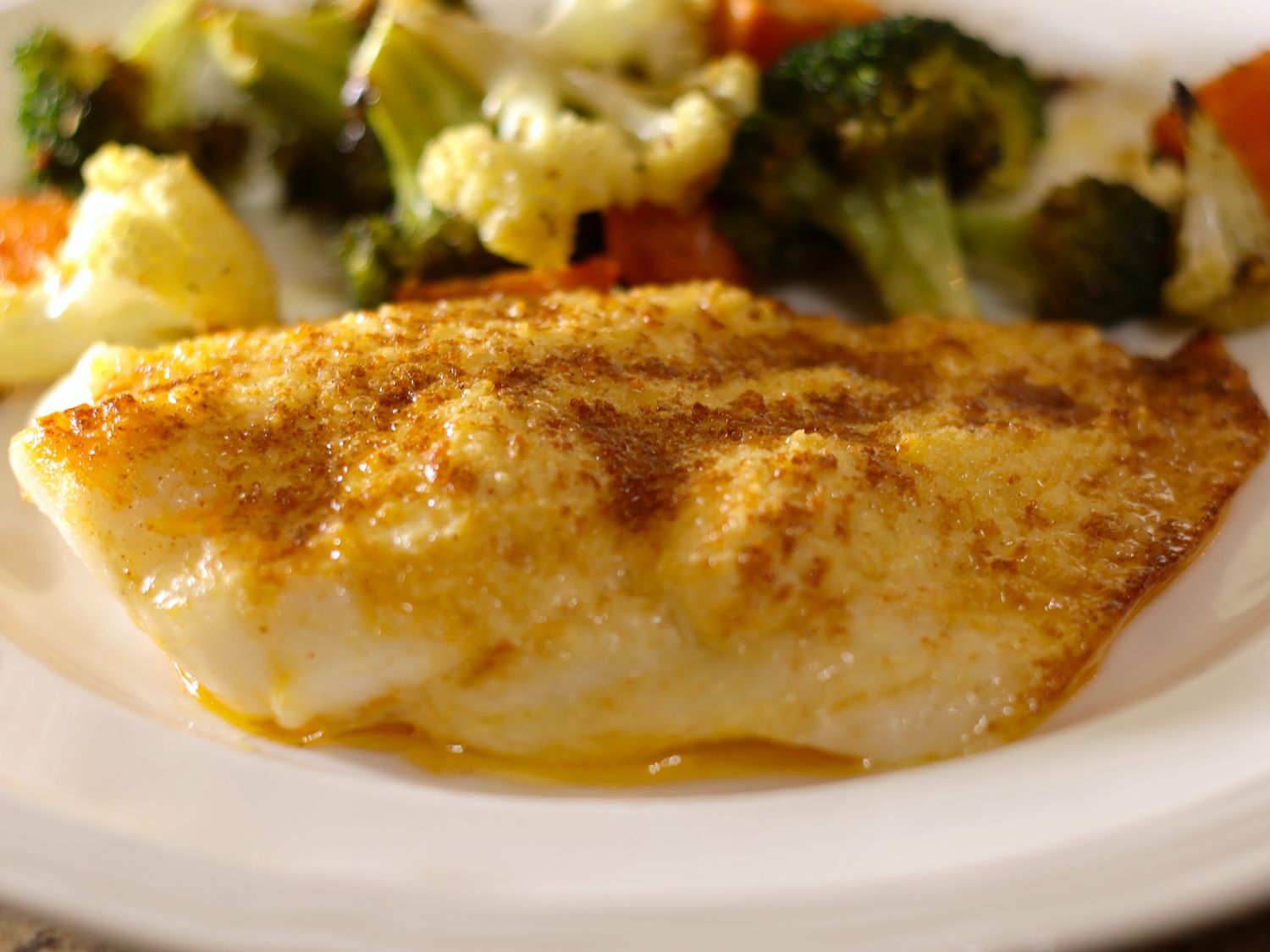 Orange roughy fillets being patted dry with paper towels on a cutting board next to a small bowl of seasoning