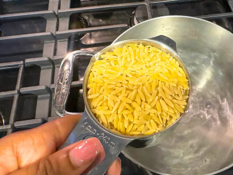 Orzo pasta simmering in a large stainless steel pot on a stovetop with gentle bubbling water