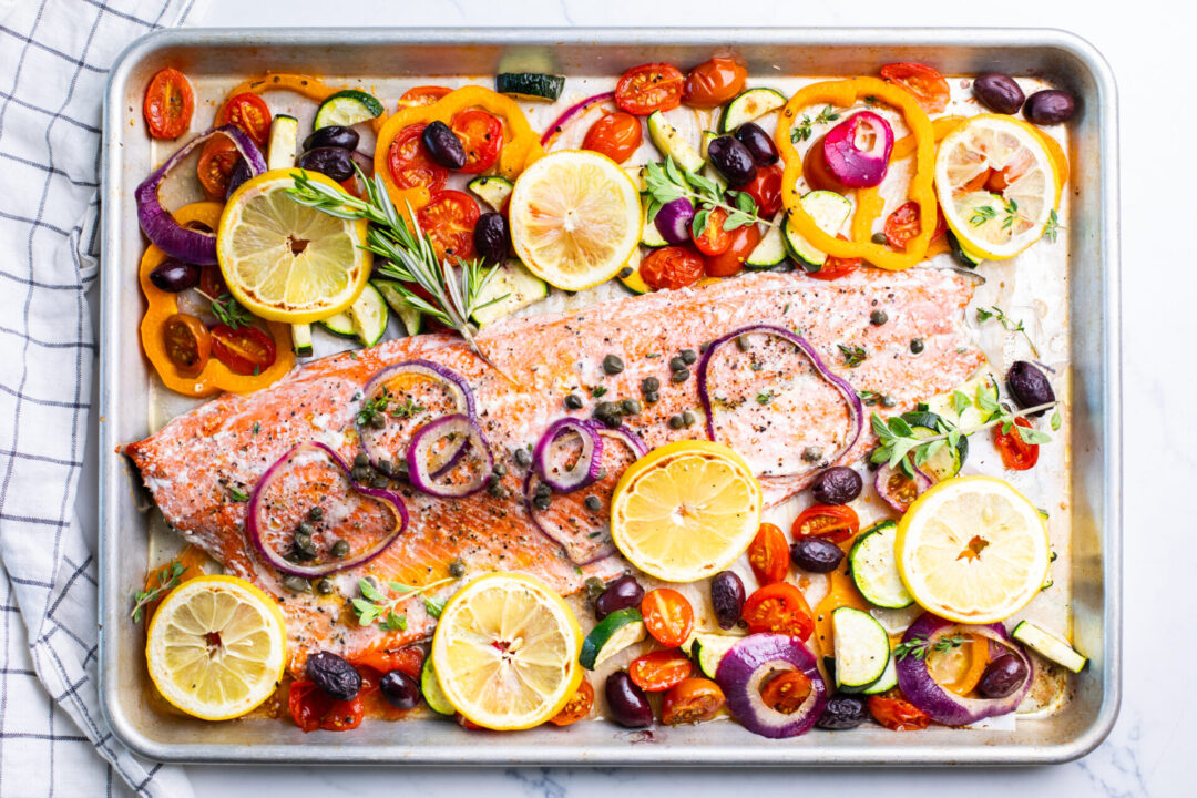 Oven-baked salmon fillets on a sheet pan with lemon slices and herbs