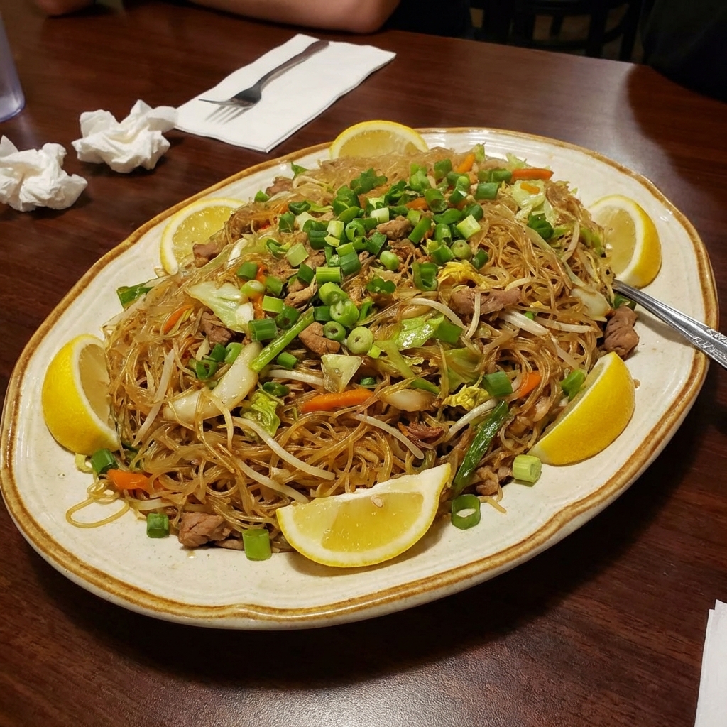 Pancit piled onto a serving platter with lemon wedges and sliced green onions