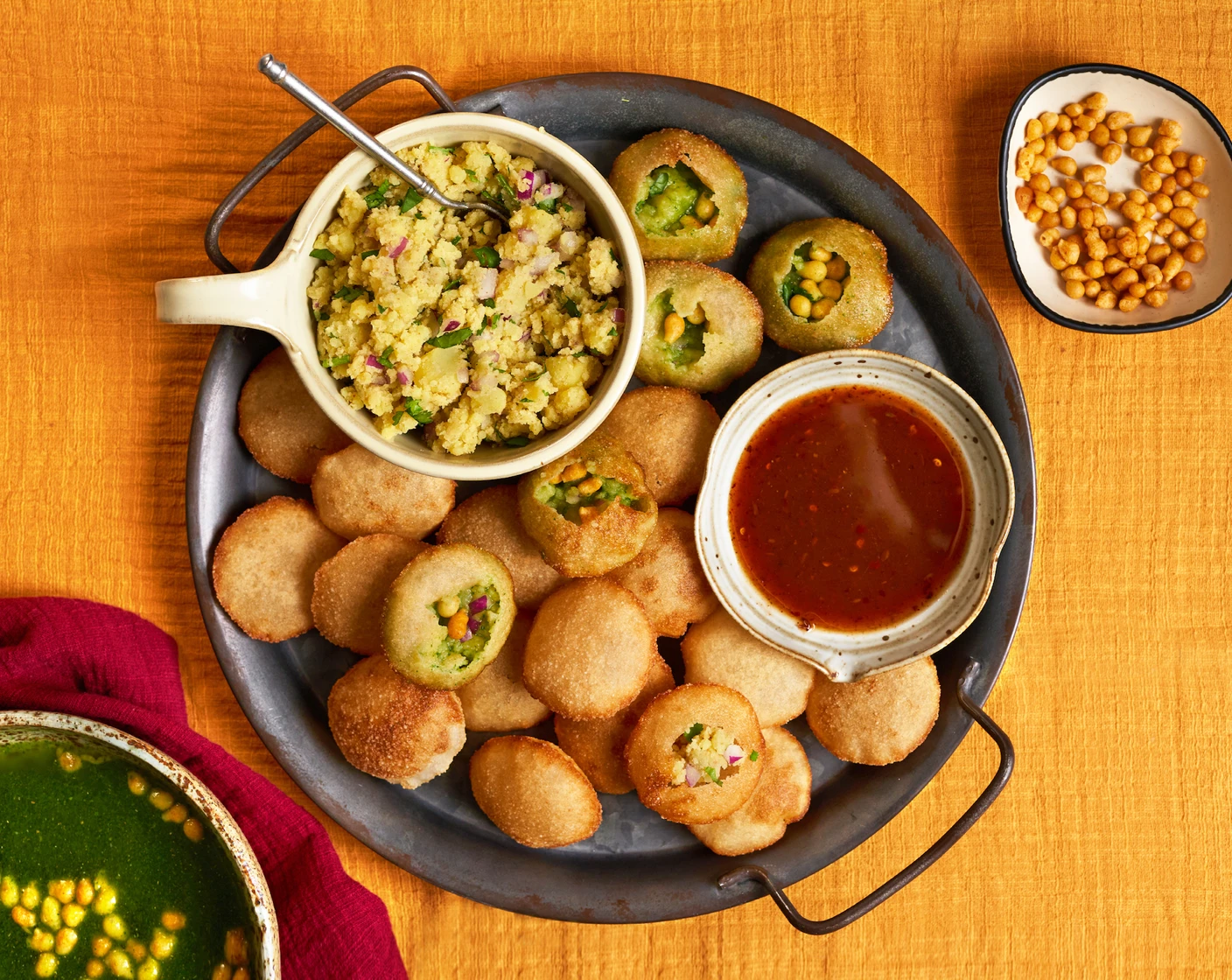 Pani puri ingredients arranged on a kitchen counter including puri shells, boiled potatoes, canned chickpeas, cilantro, mint, tamarind, spices, and small bowls