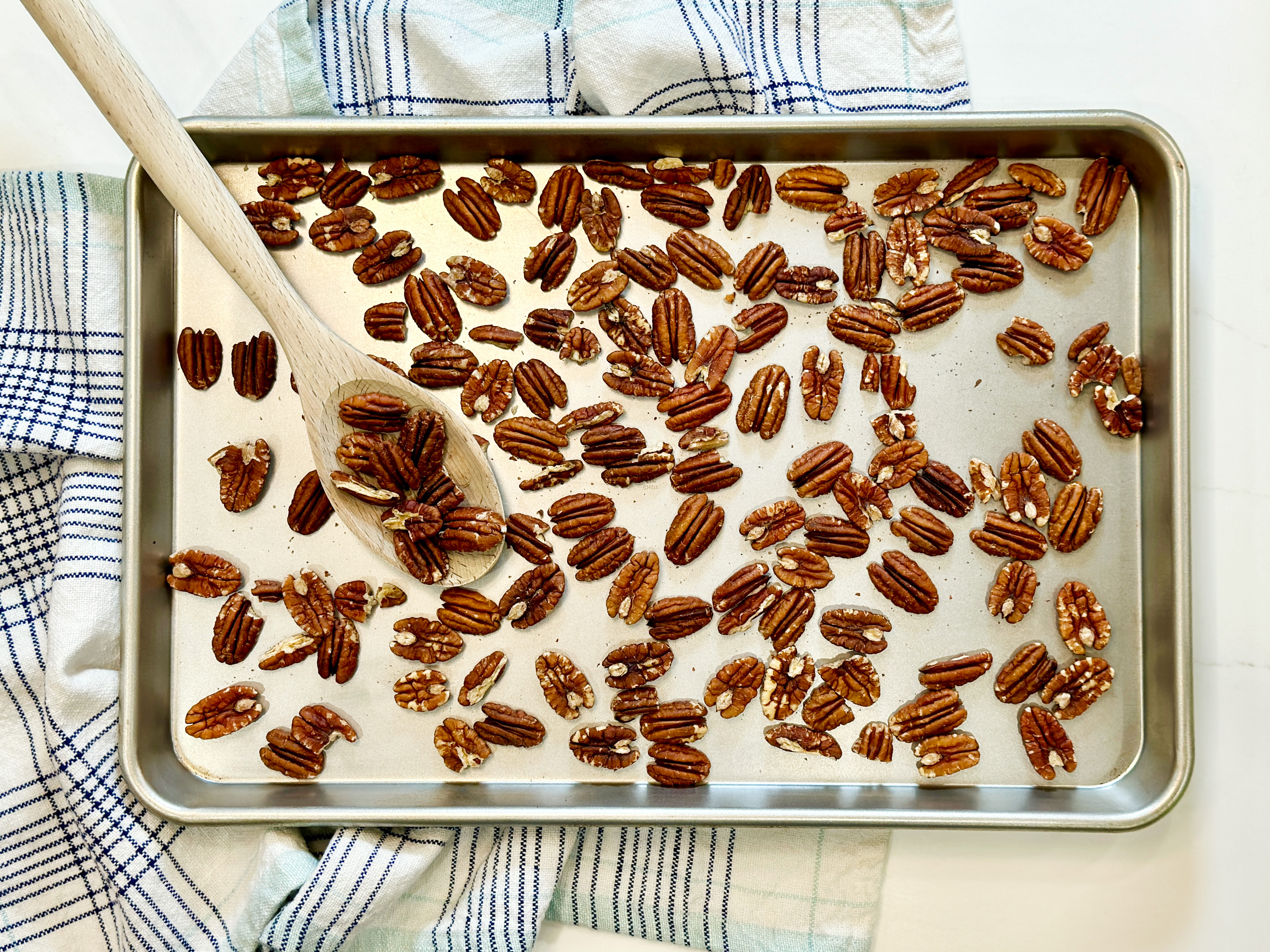 Pecan halves toasted on a rimmed baking sheet in a home kitchen, lightly browned and fragrant, ready to be added to pie filling